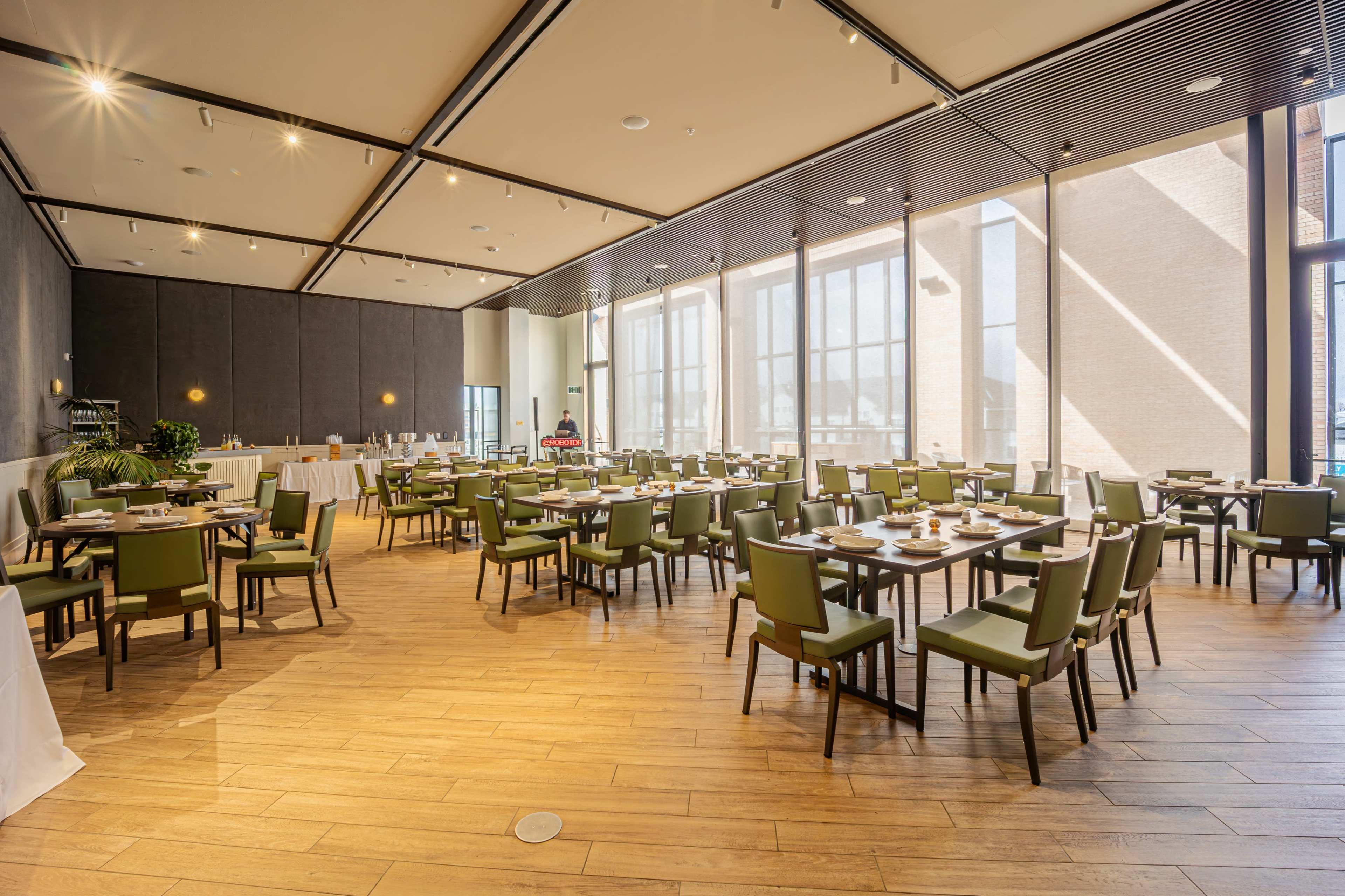 The image shows a spacious restaurant interior with wooden floors, large windows allowing natural light, and neatly arranged tables and chairs.
