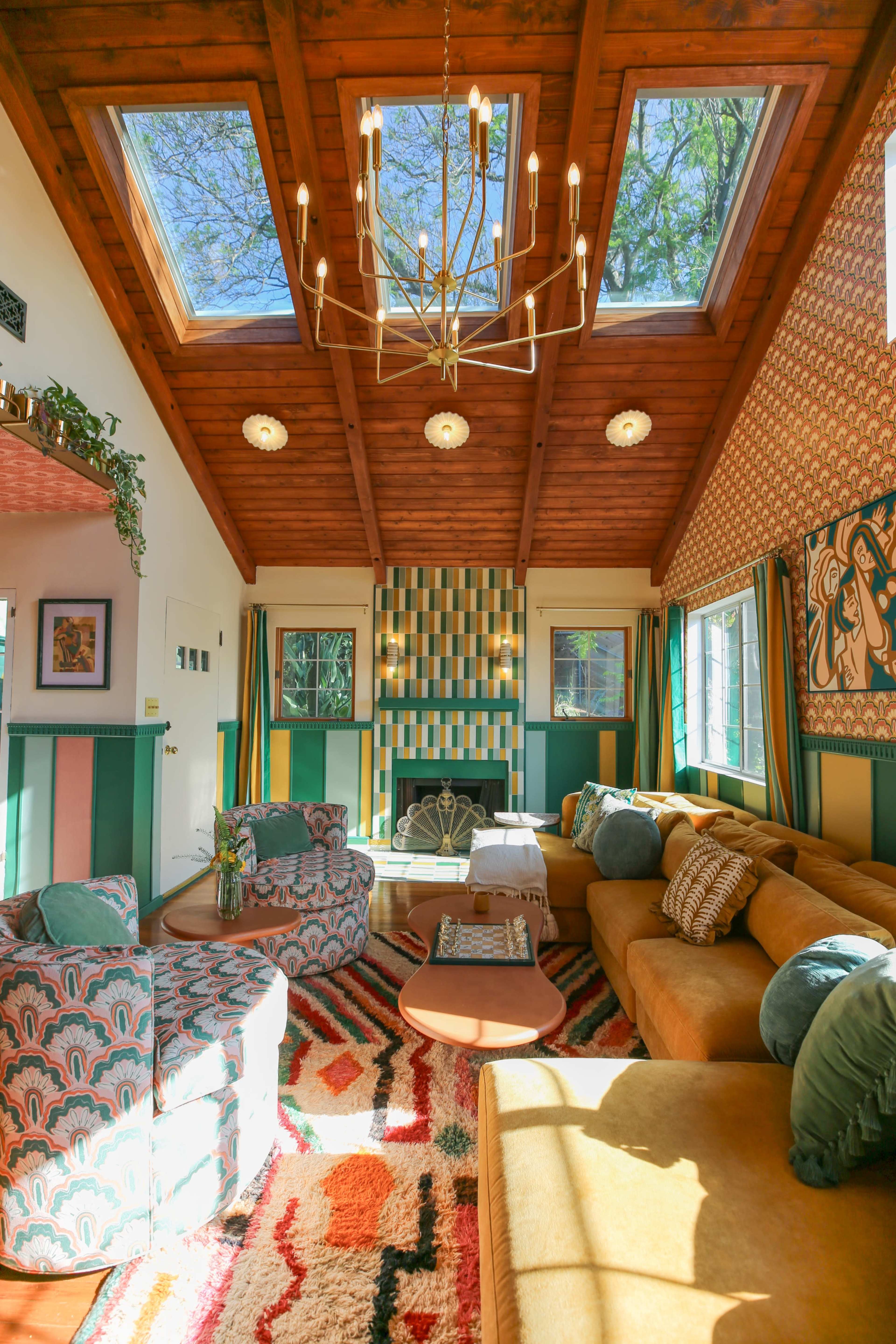 The living room features a high, wooden ceiling with skylights, colorful patterned walls, and a large sectional sofa arranged around a central coffee table.