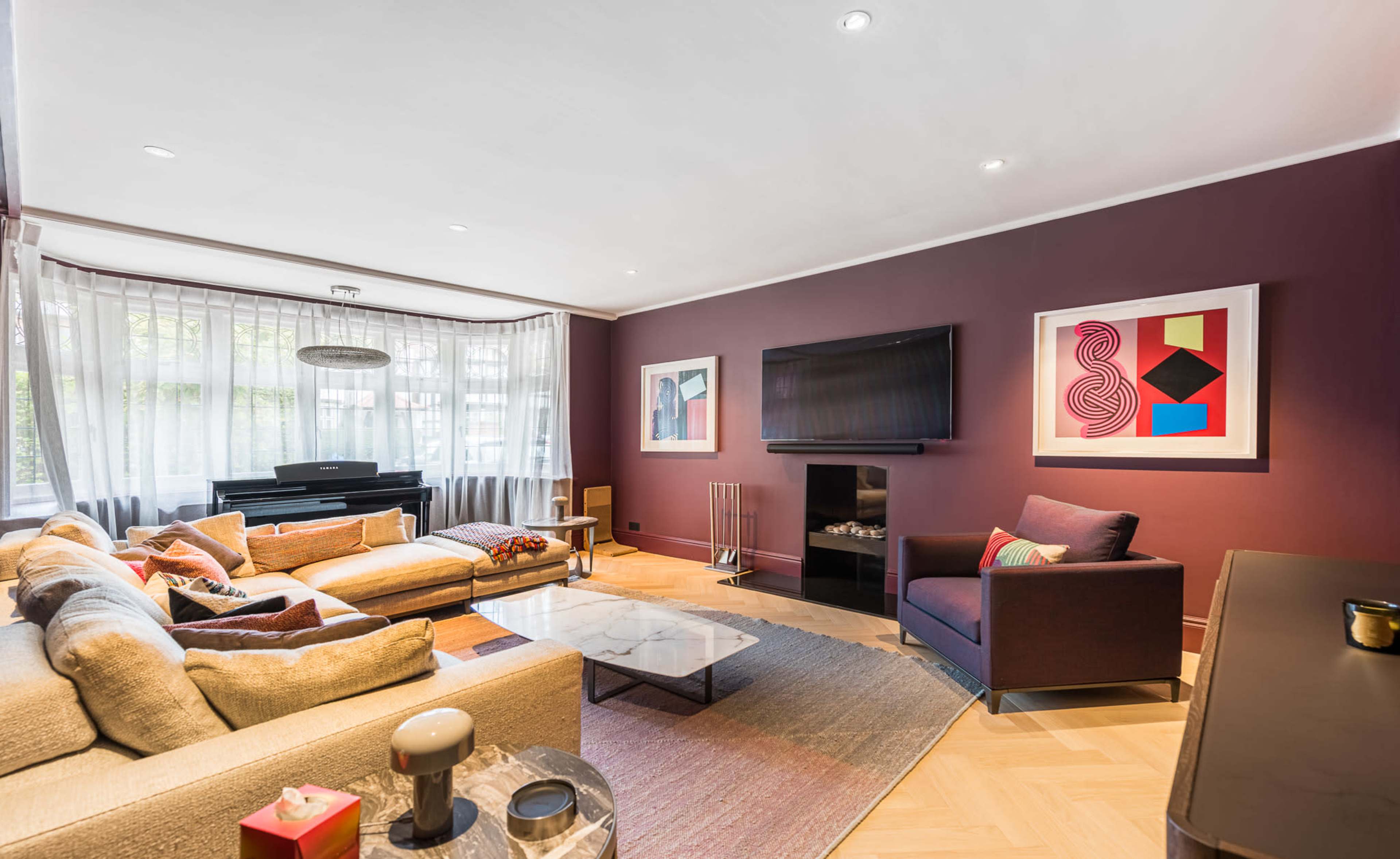 The image shows a modern living room featuring a sectional sofa, a coffee table, a television mounted on the wall, and artwork displayed on the walls.