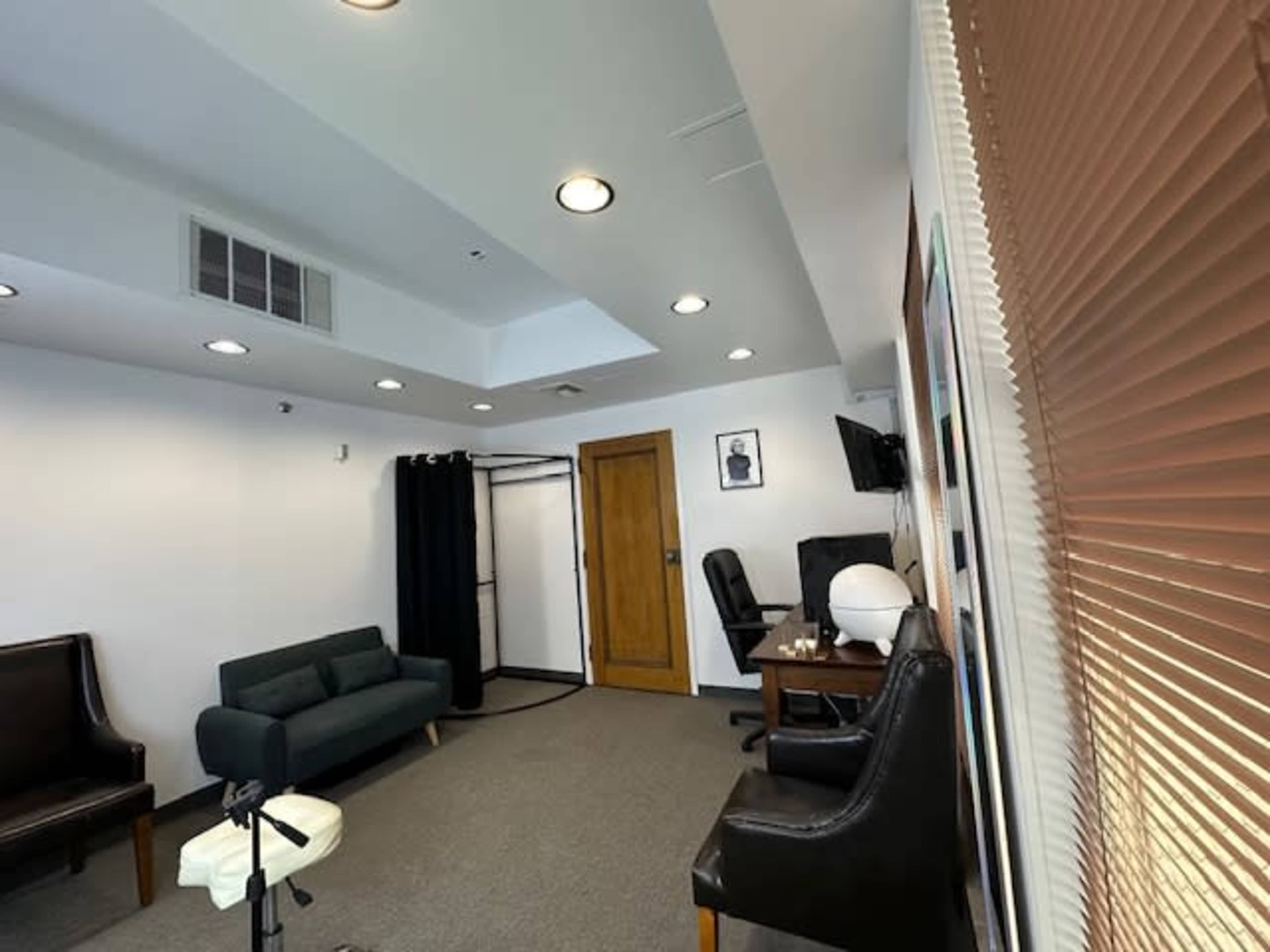 The room features a couch, two chairs, a desk with a monitor, and a closet area, all arranged under ceiling lights.
