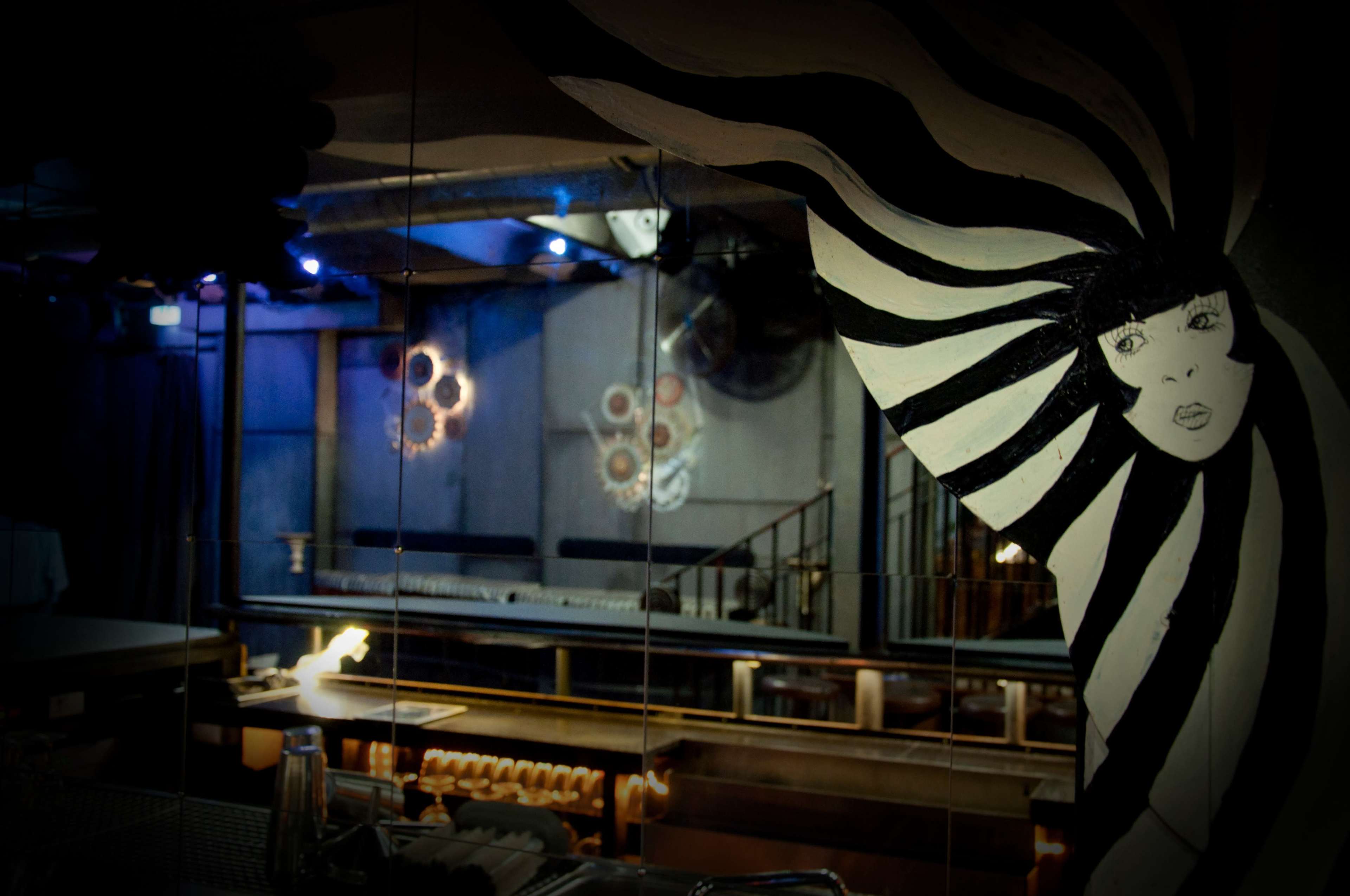 A mirrored wall reflects a stylish interior of a restaurant with black and white artwork, visible seating, and decorative elements.