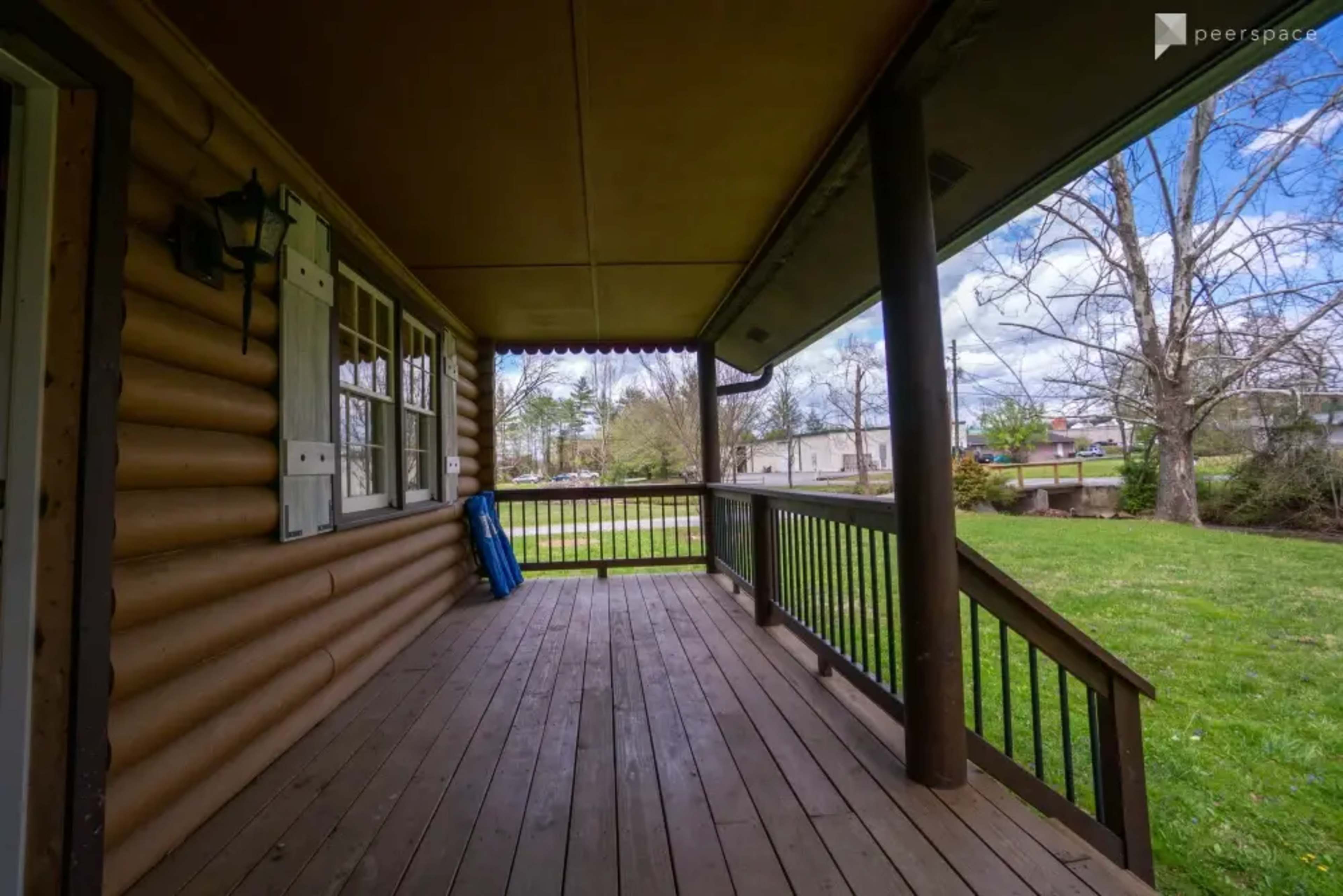 A wooden porch with a view of a grassy area and trees under a partly cloudy sky.