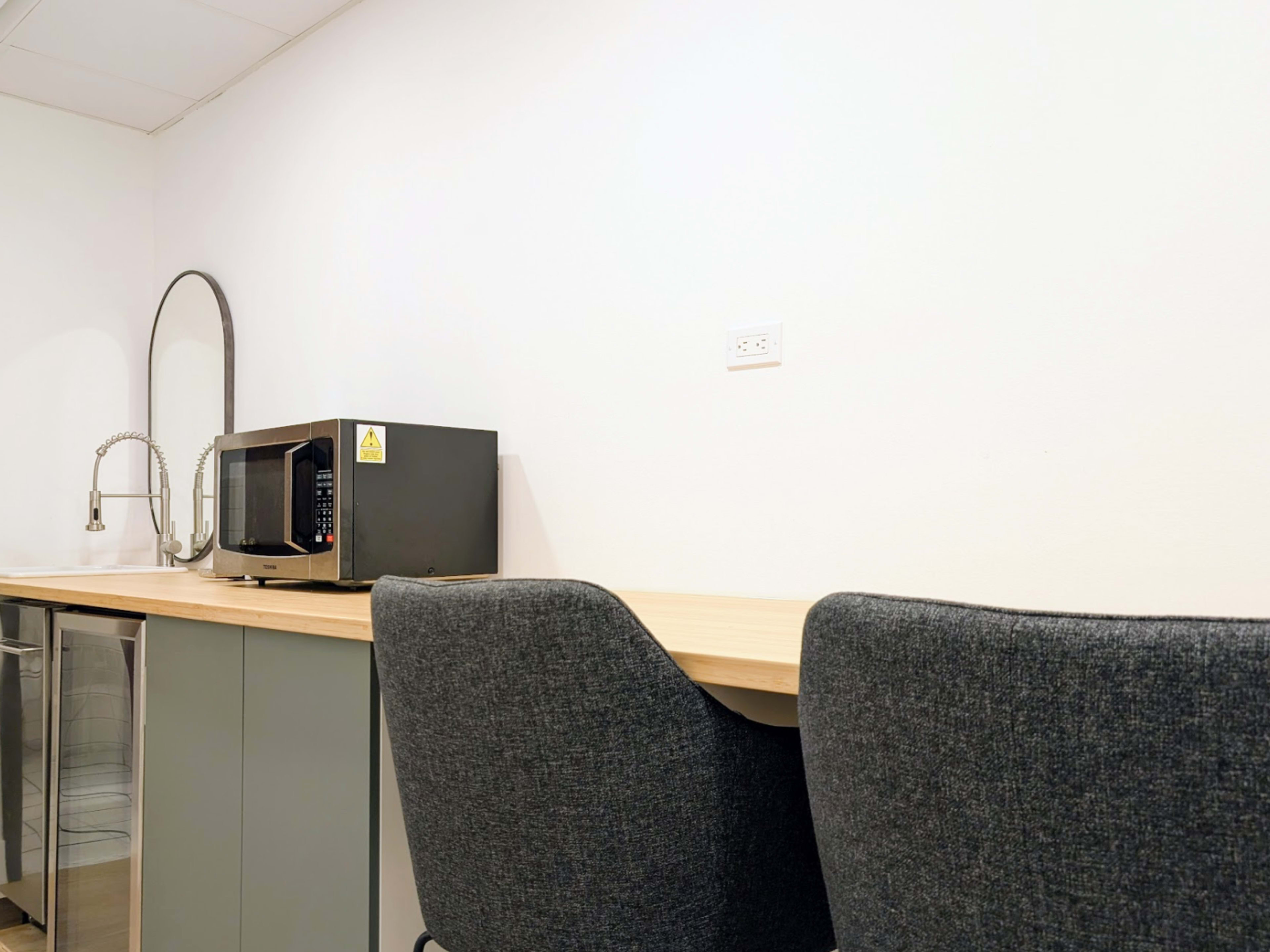 A kitchen area features a microwave on a countertop next to two upholstered chairs and a mirror on the wall.
