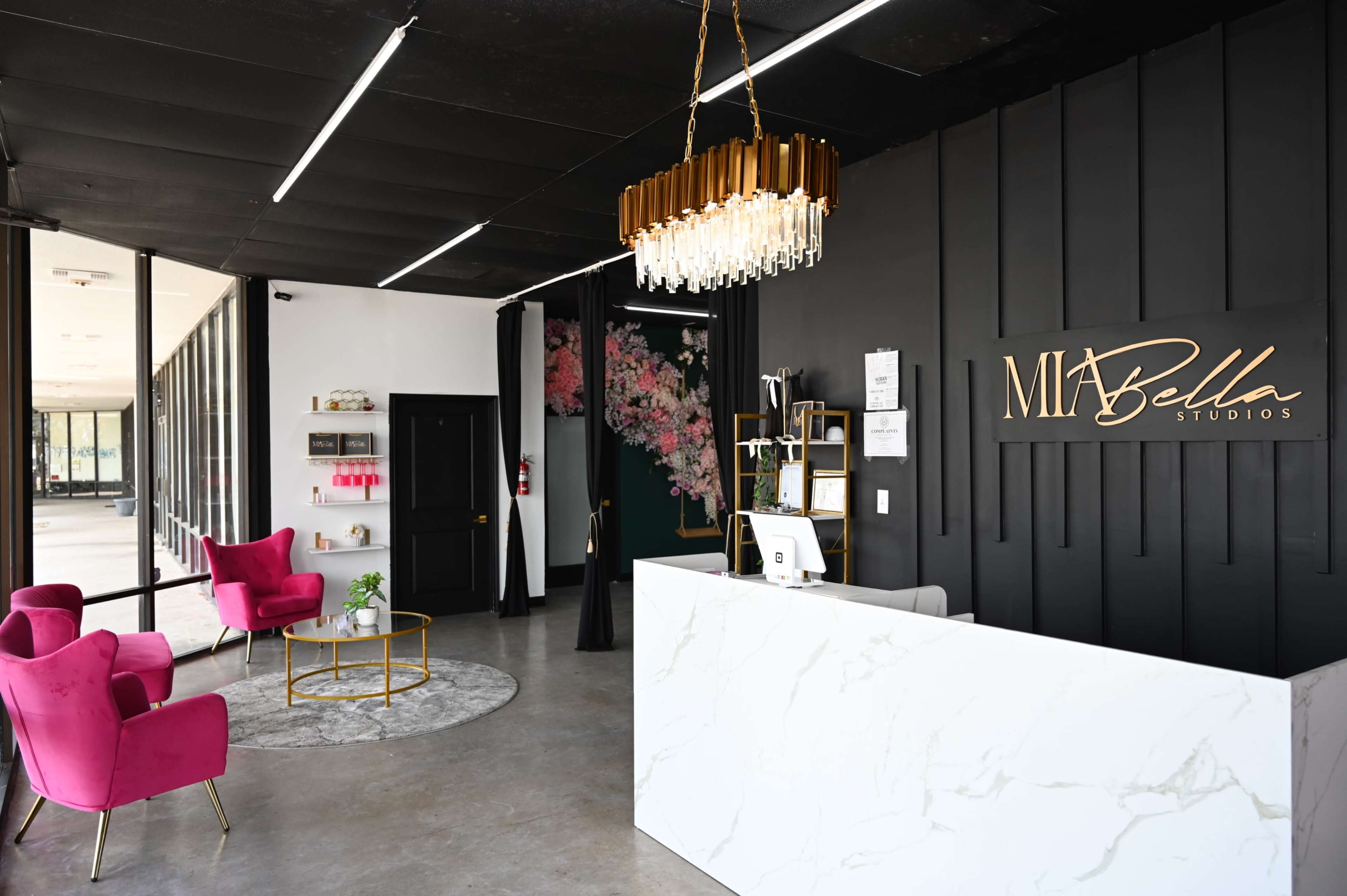 A modern reception area with a marble front desk, pink seating, a circular rug, and large glass windows.
