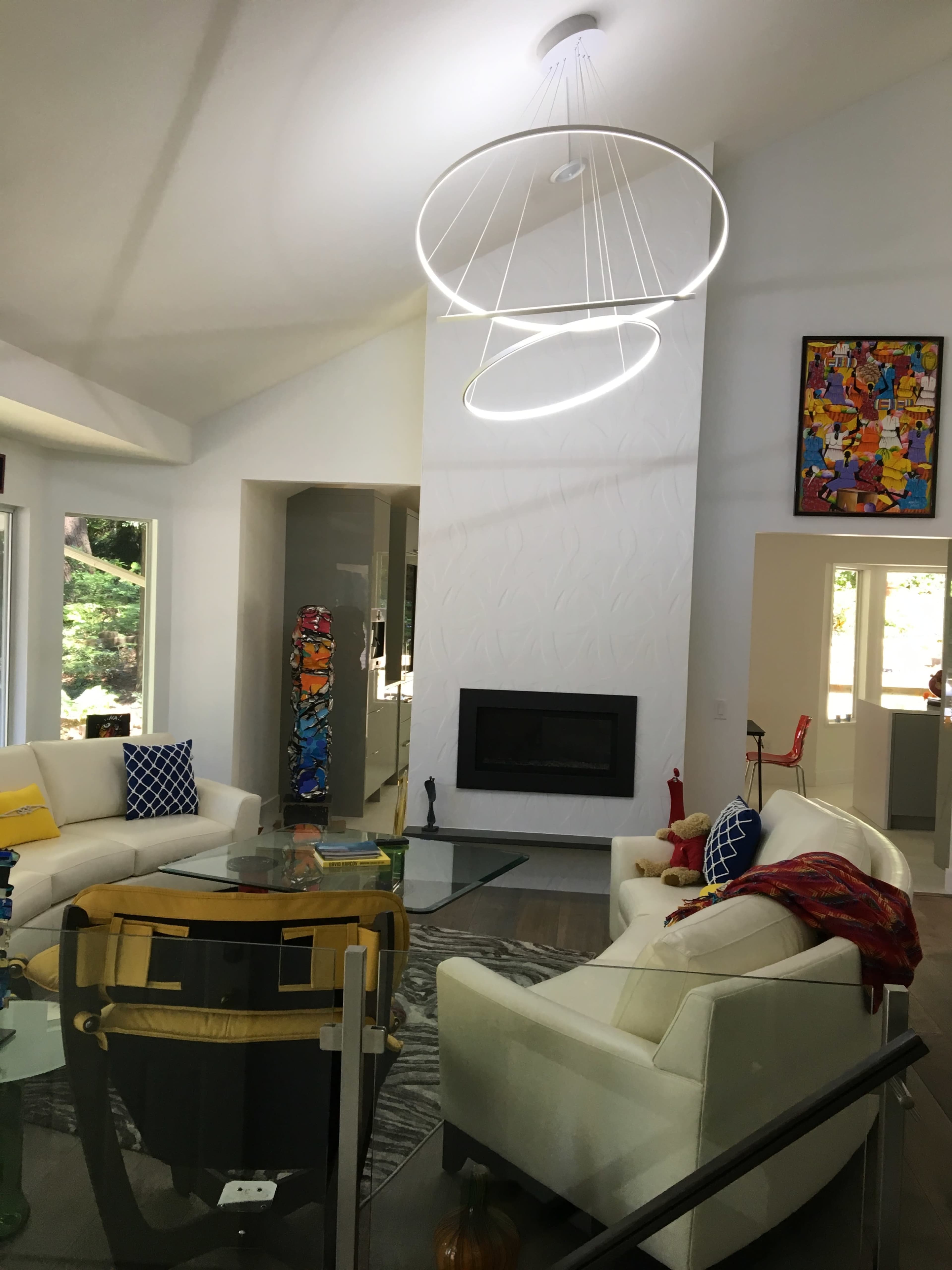 A modern living room with a circular light fixture, a fireplace, and white sofas arranged around a glass coffee table.