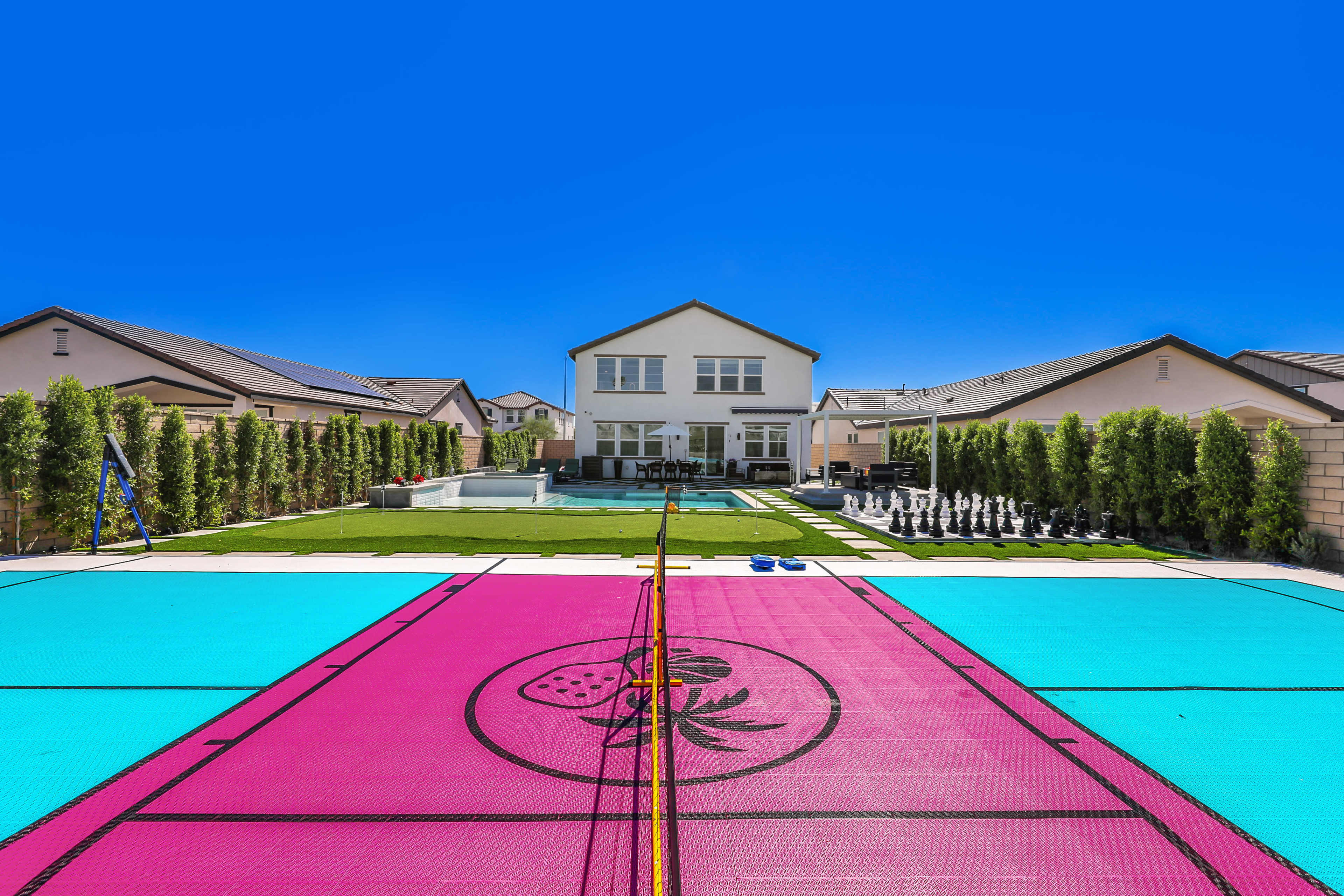 The image shows a backyard with a swimming pool, a grass area, and a brightly colored multi-sport court with a house in the background.