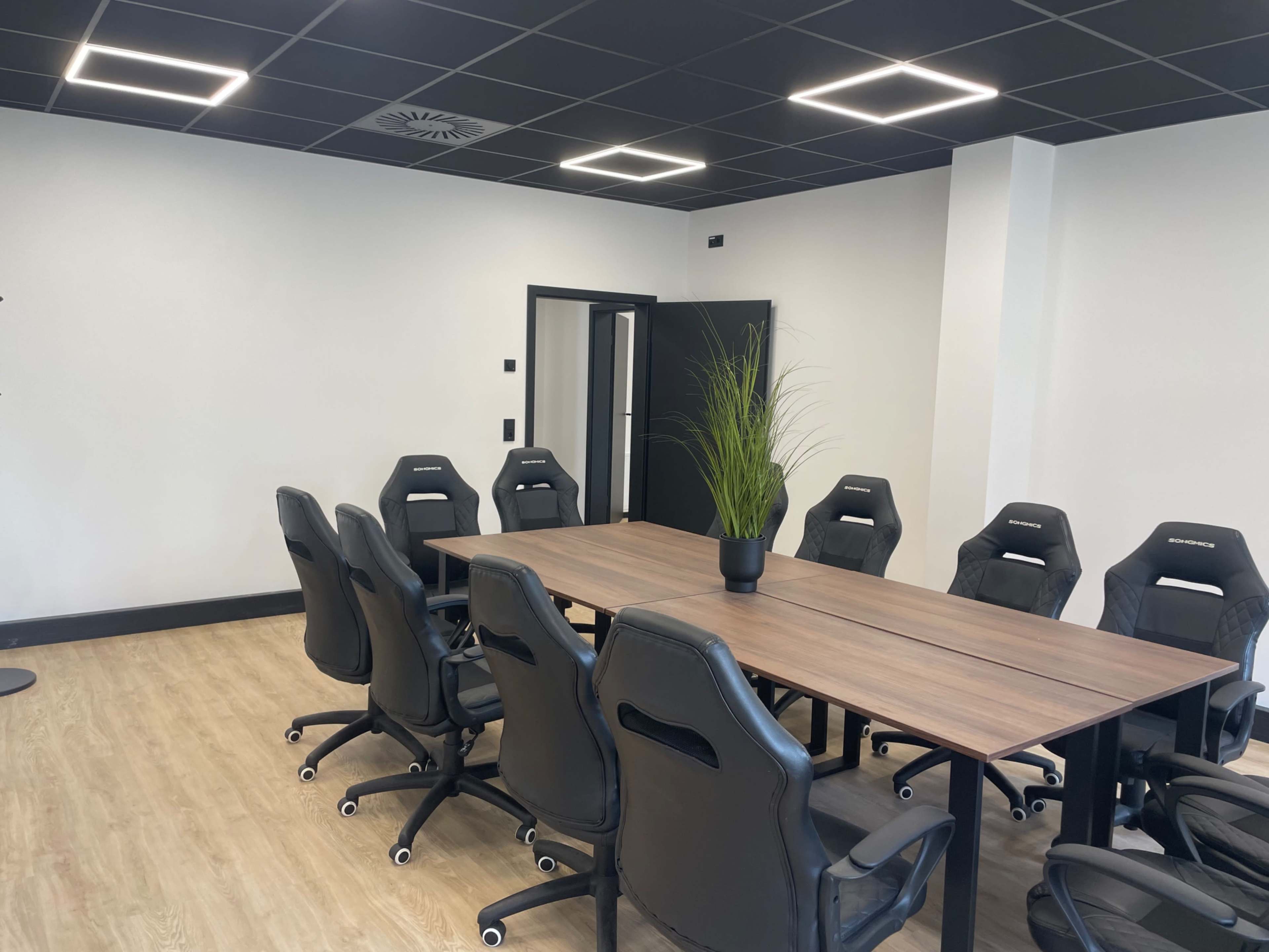 The image shows a modern conference room with a large wooden table surrounded by ergonomic black chairs and minimalistic decor.