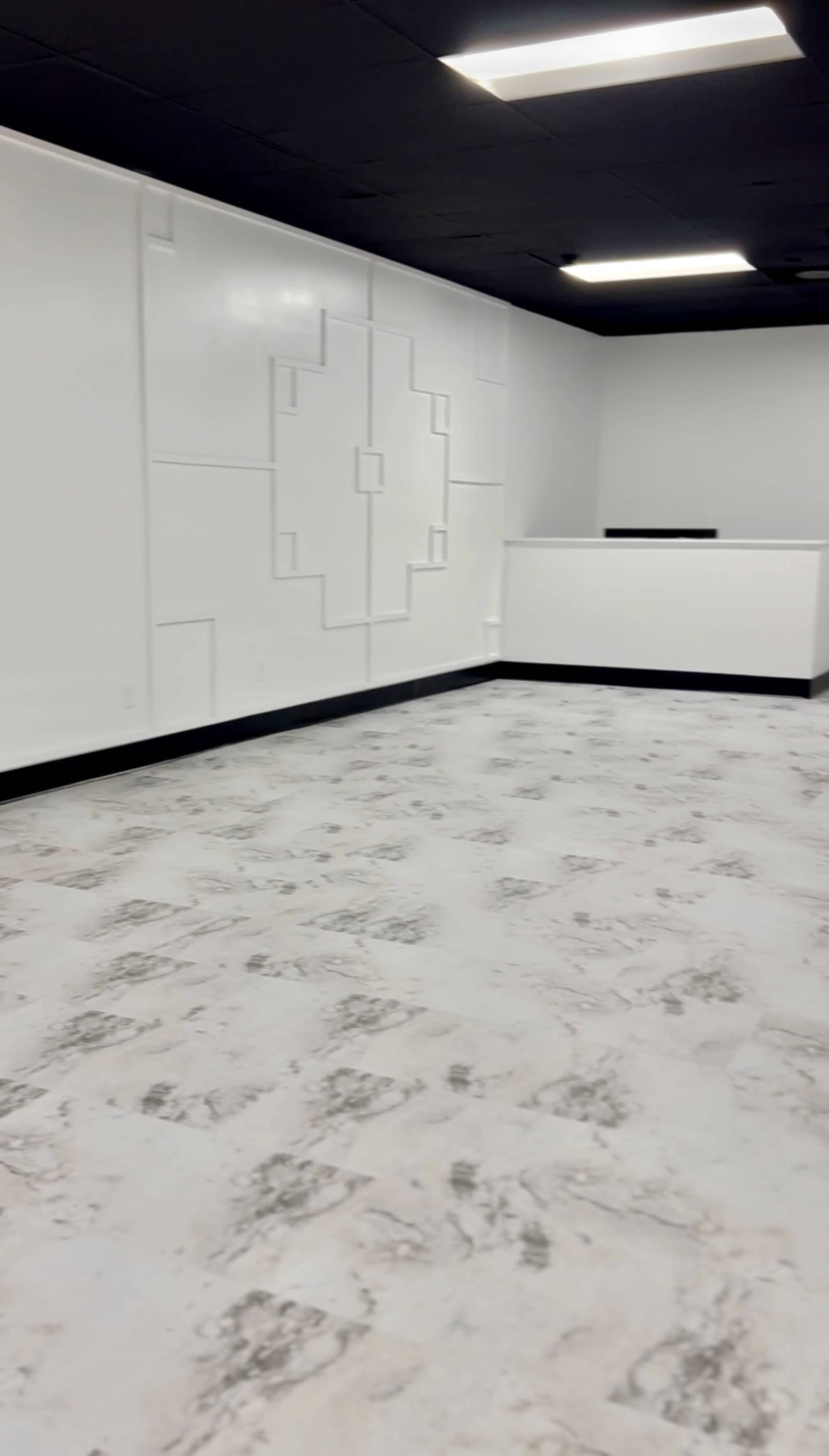 A minimalistic, empty room with white walls and a patterned design, featuring a reception-style counter against one wall.