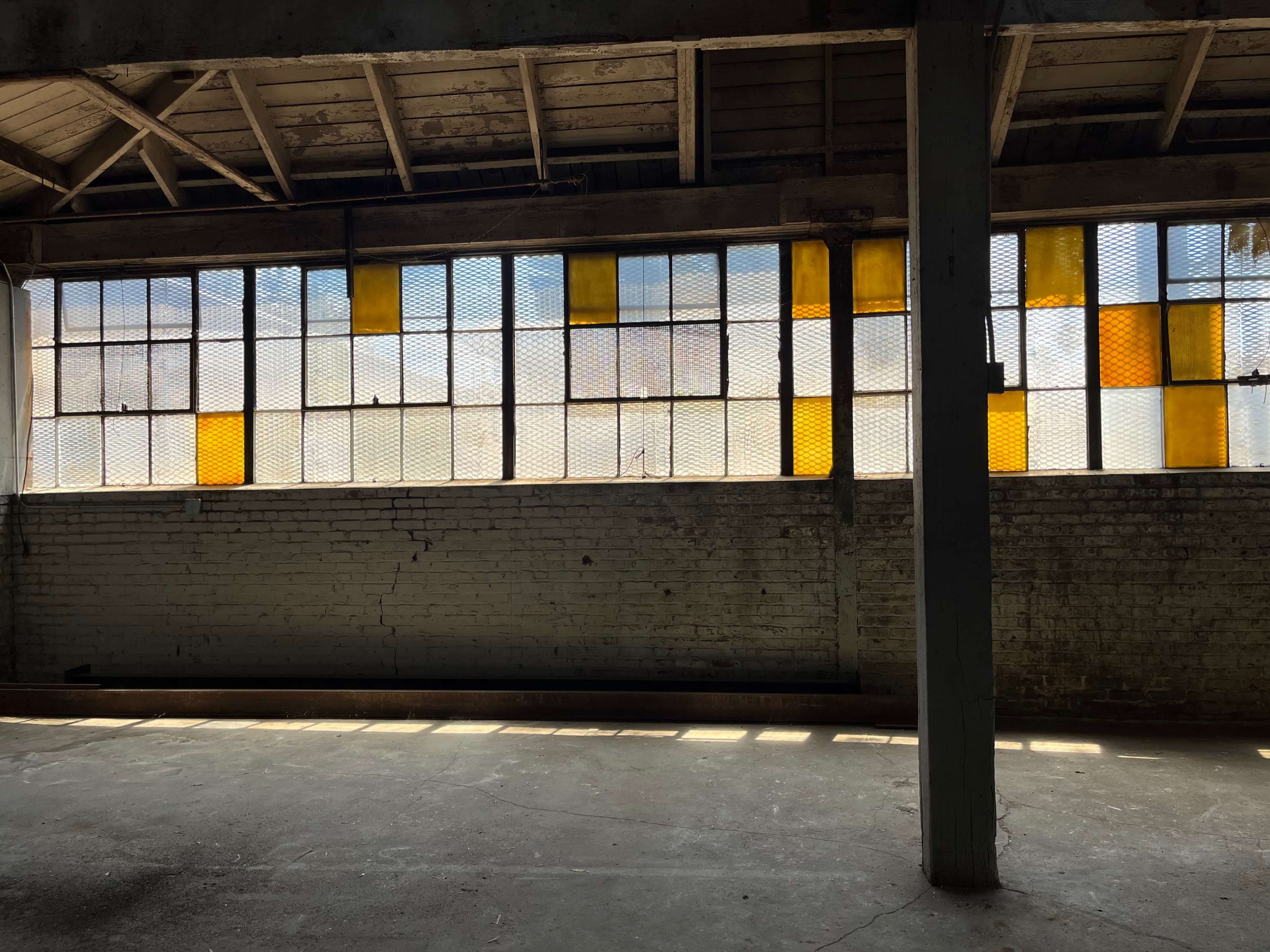 An industrial interior with a long window featuring yellow and clear panes, casting shadows on the concrete floor.