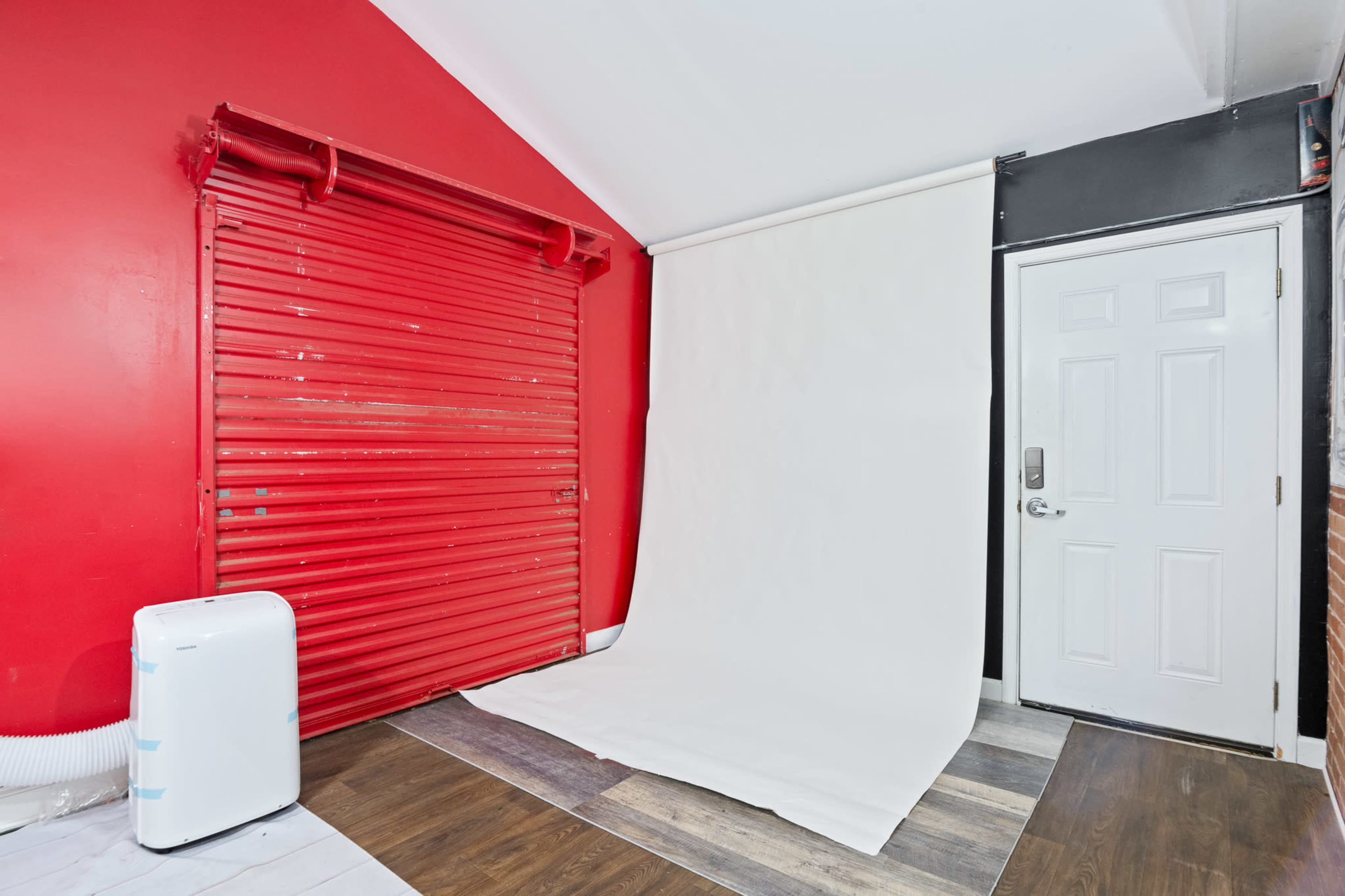 The image features a room with a red wall, a white backdrop on the floor, and a door on one side, complemented by a white appliance.