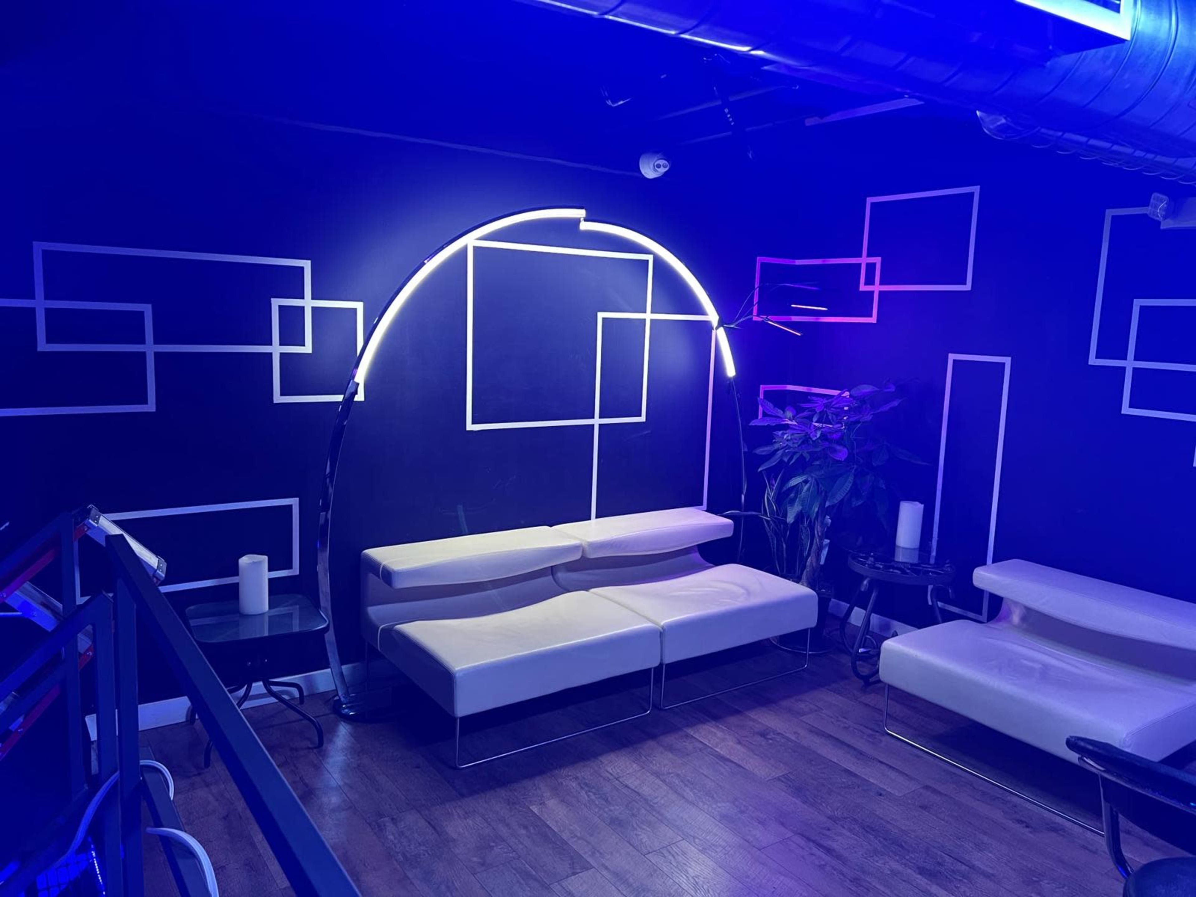 The scene shows a lounge area with modern white seating, neon lighting, and geometric wall decorations against a dark background.