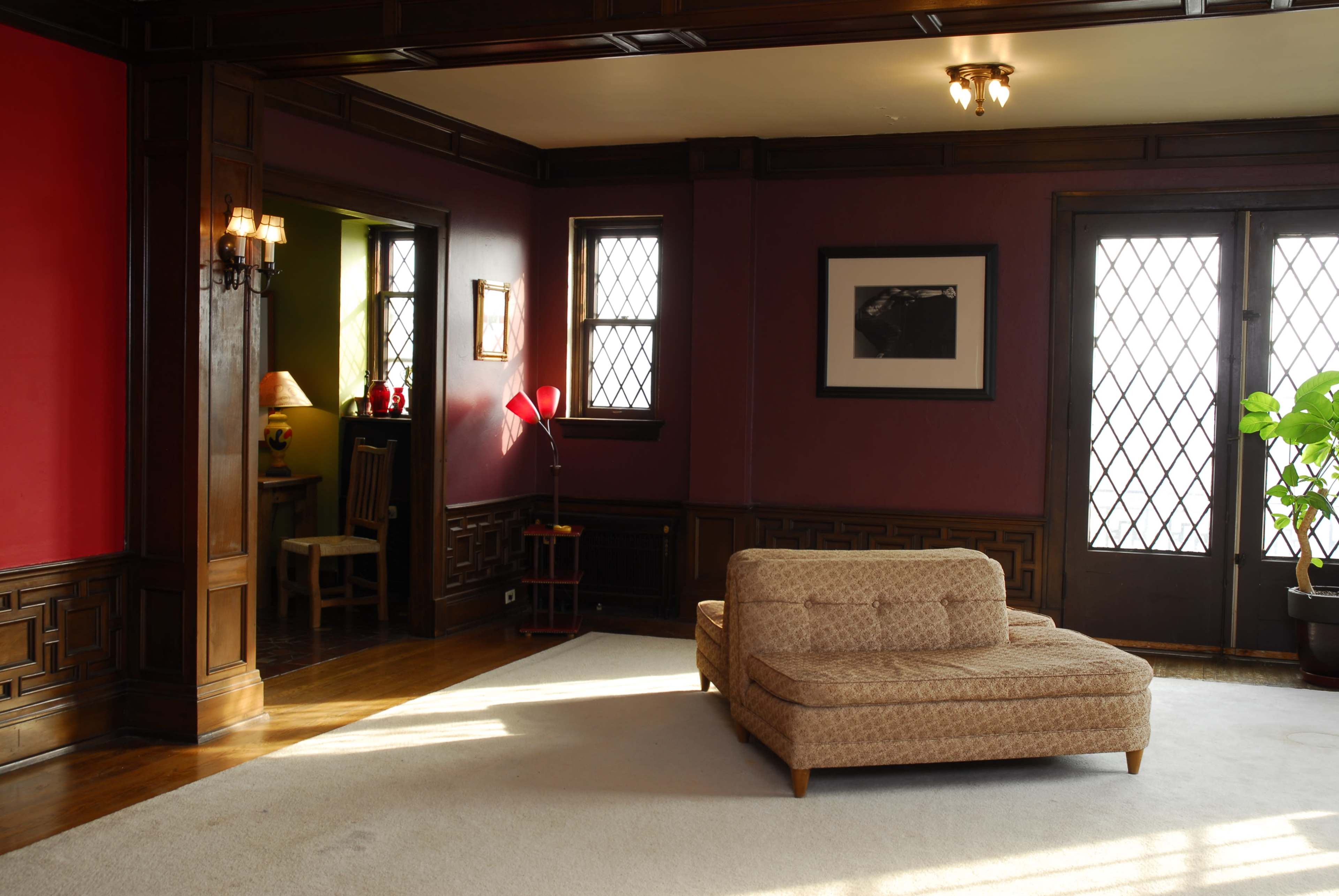 A spacious living room features a beige sectional sofa on a light rug, wooden accents, and large windows that provide natural light.