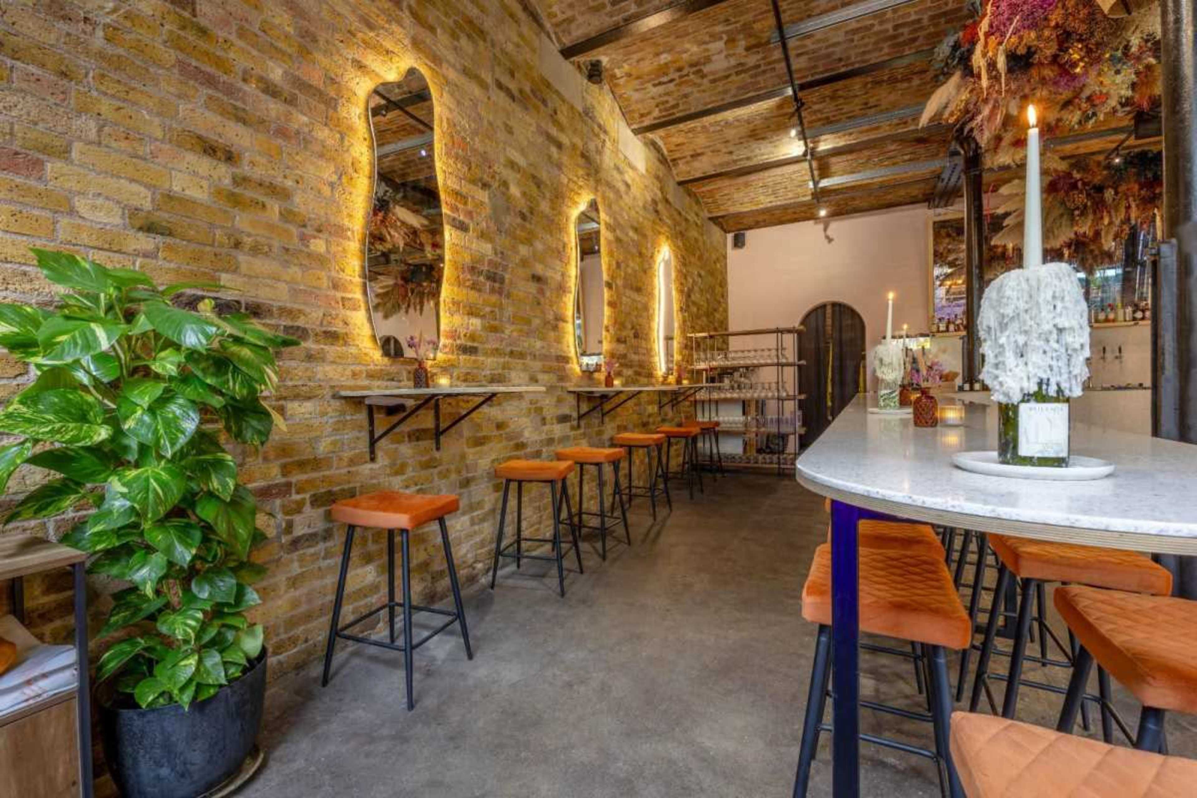 A modern restaurant interior with exposed brick walls, a long white marble bar with high stools, and decorative elements like candles and plants.