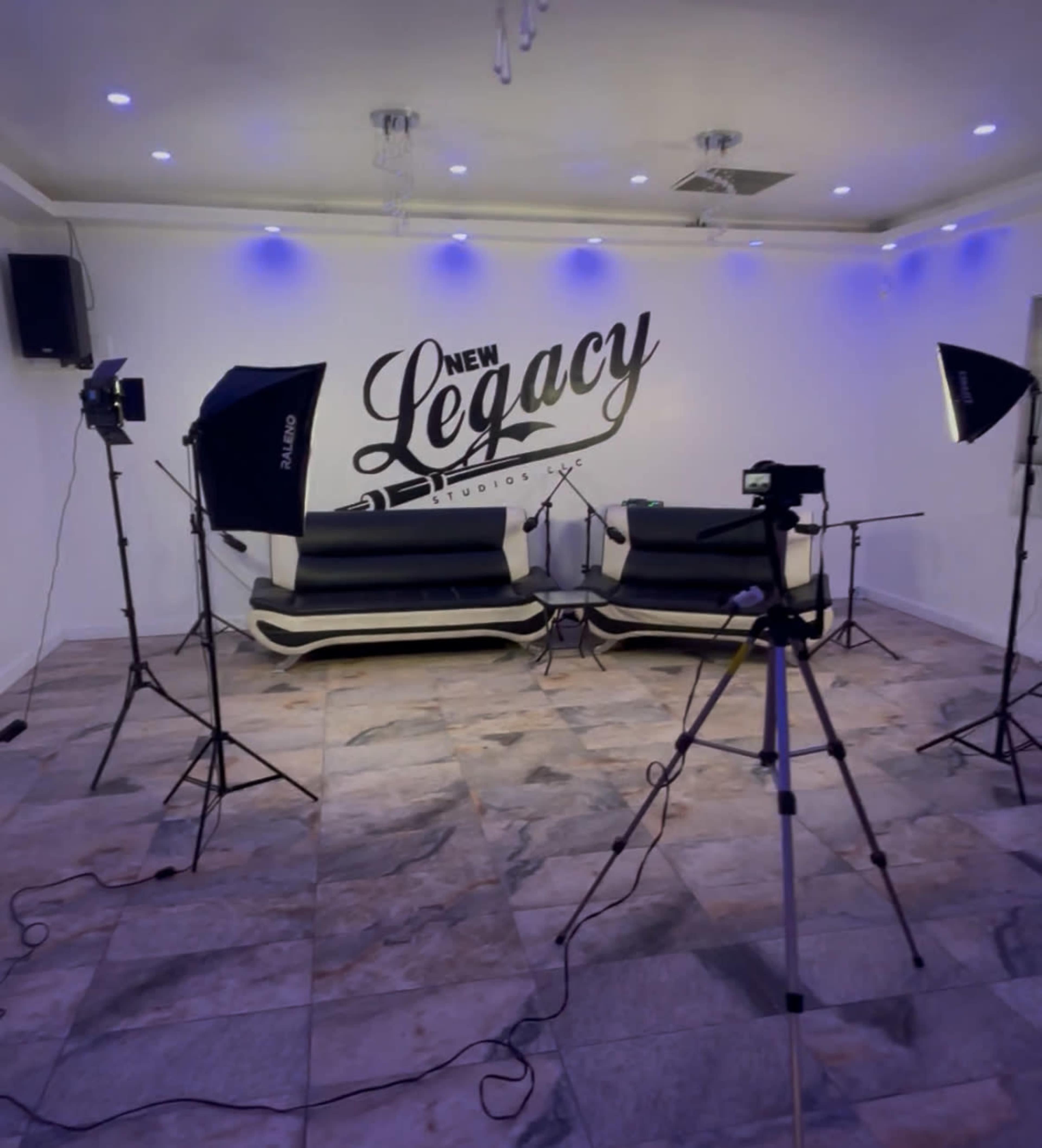 The image shows a recording studio with two black couches, bright lighting, and various photography equipment arranged around the space.