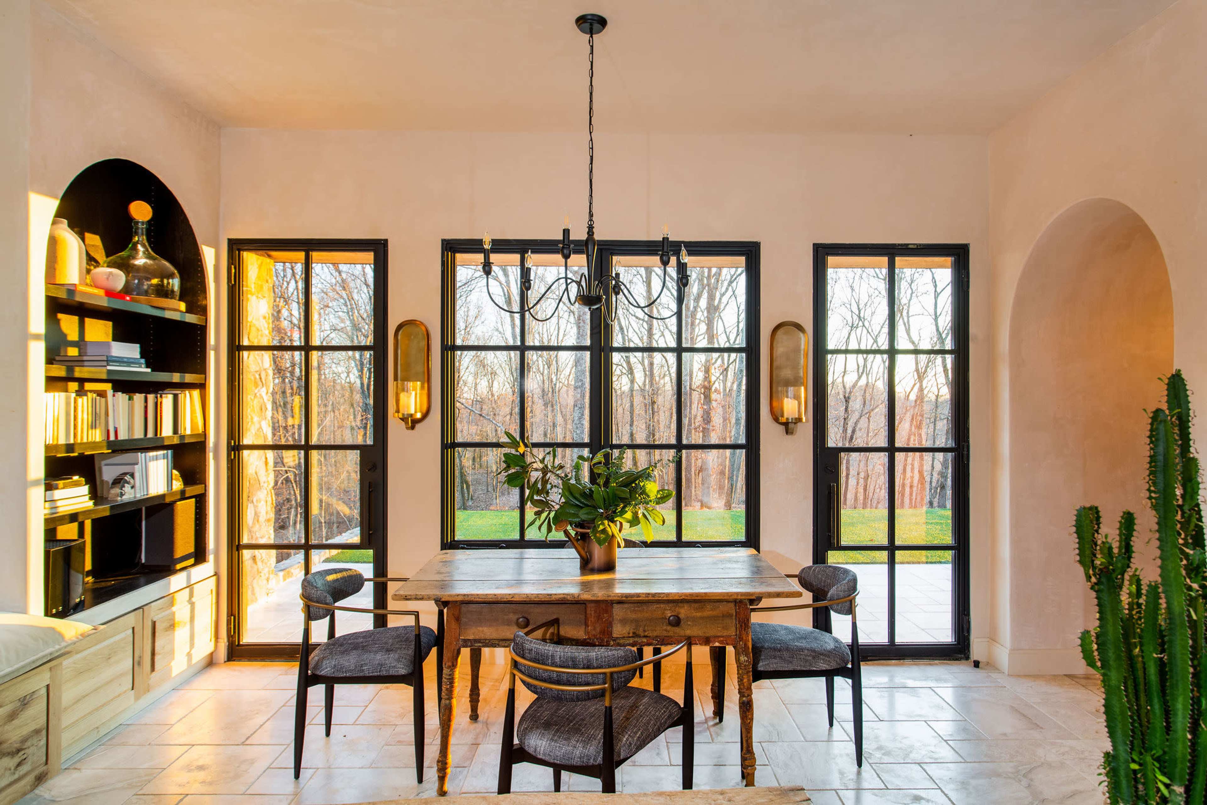 A dining area features a wooden table surrounded by chairs, with large windows allowing natural light to illuminate the space.