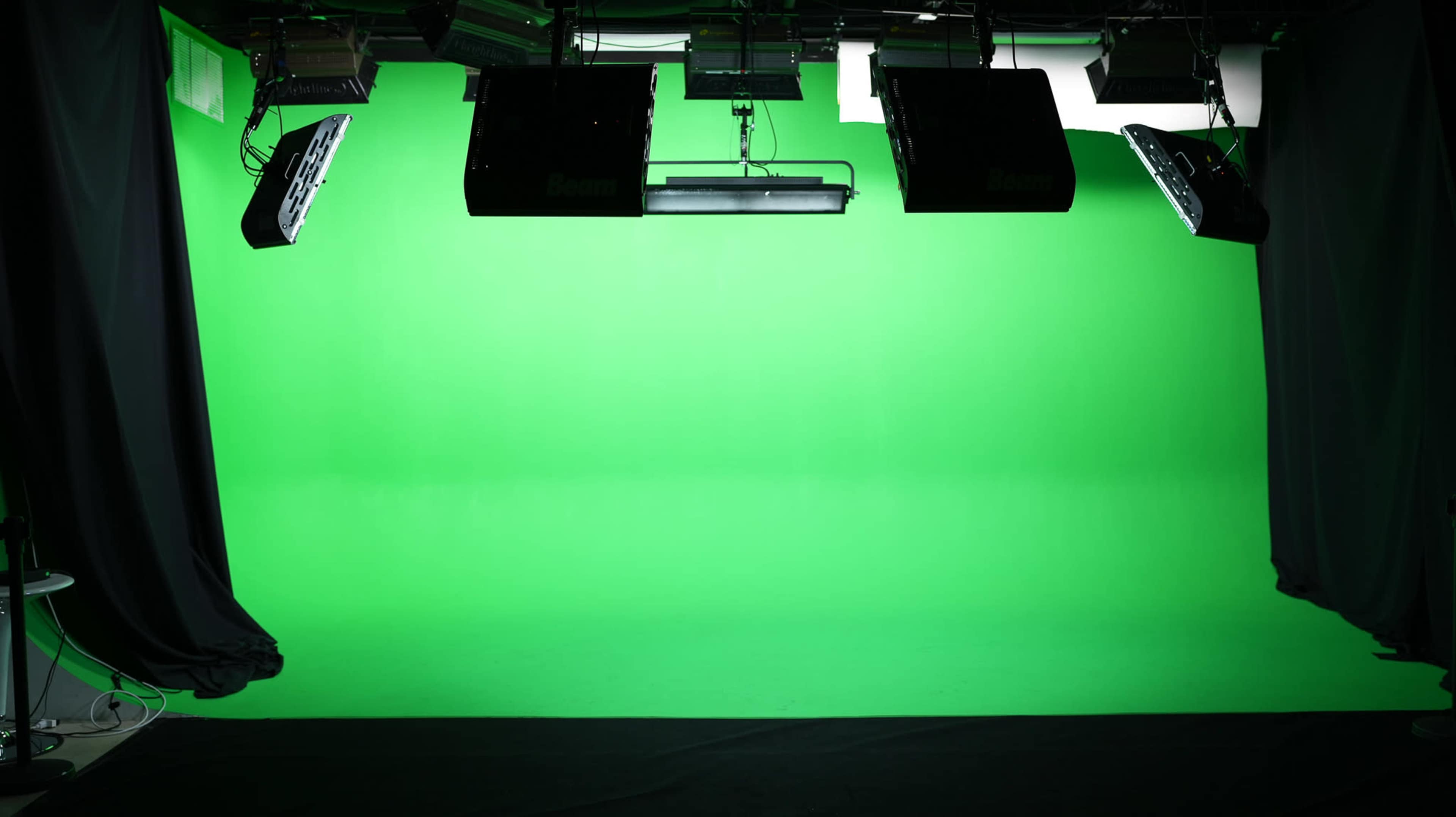 A studio setup with a bright green backdrop and overhead lighting fixtures.
