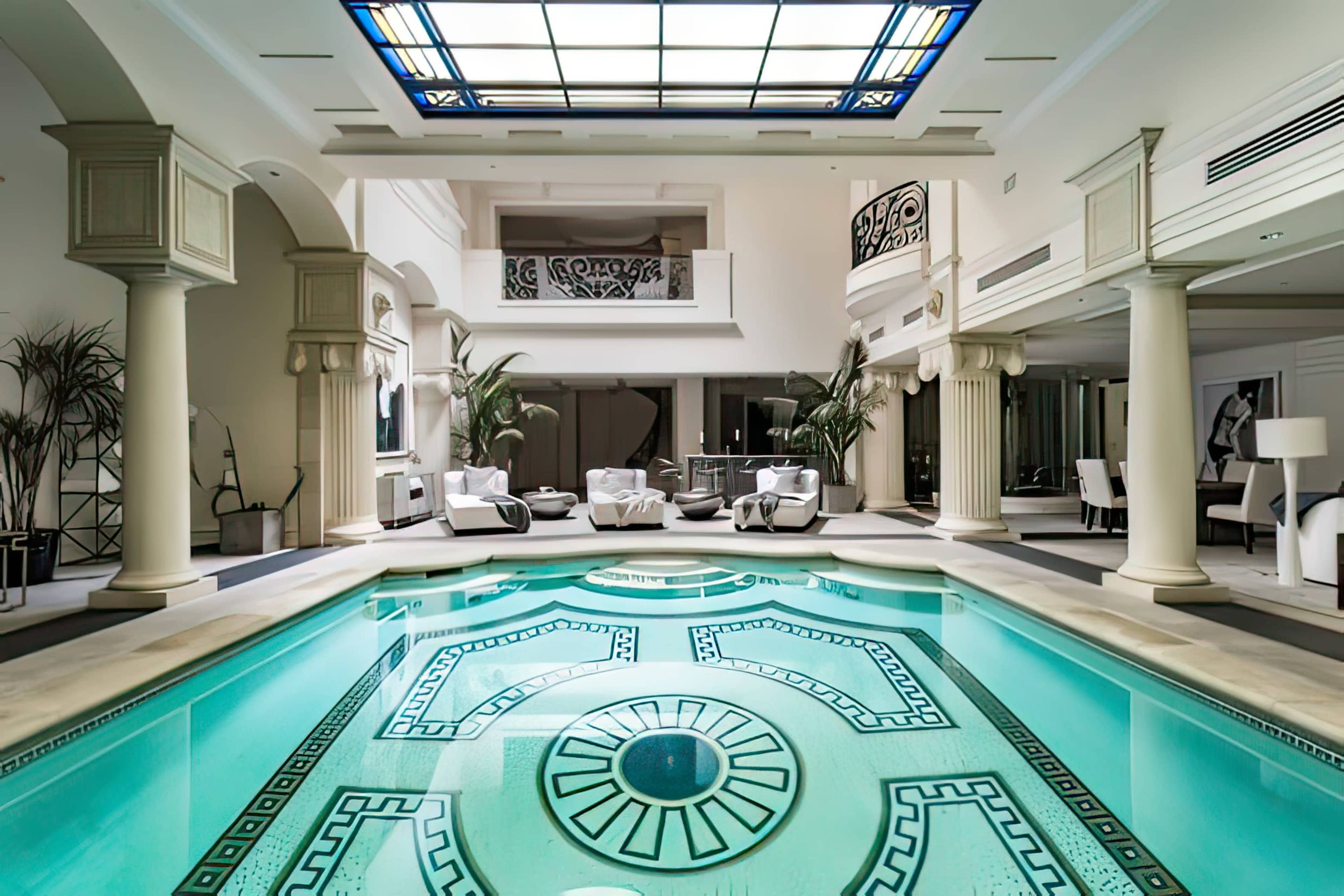 A luxurious indoor pool surrounded by elegant columns and modern furnishings, with ample natural light filtering in from a skylight.
