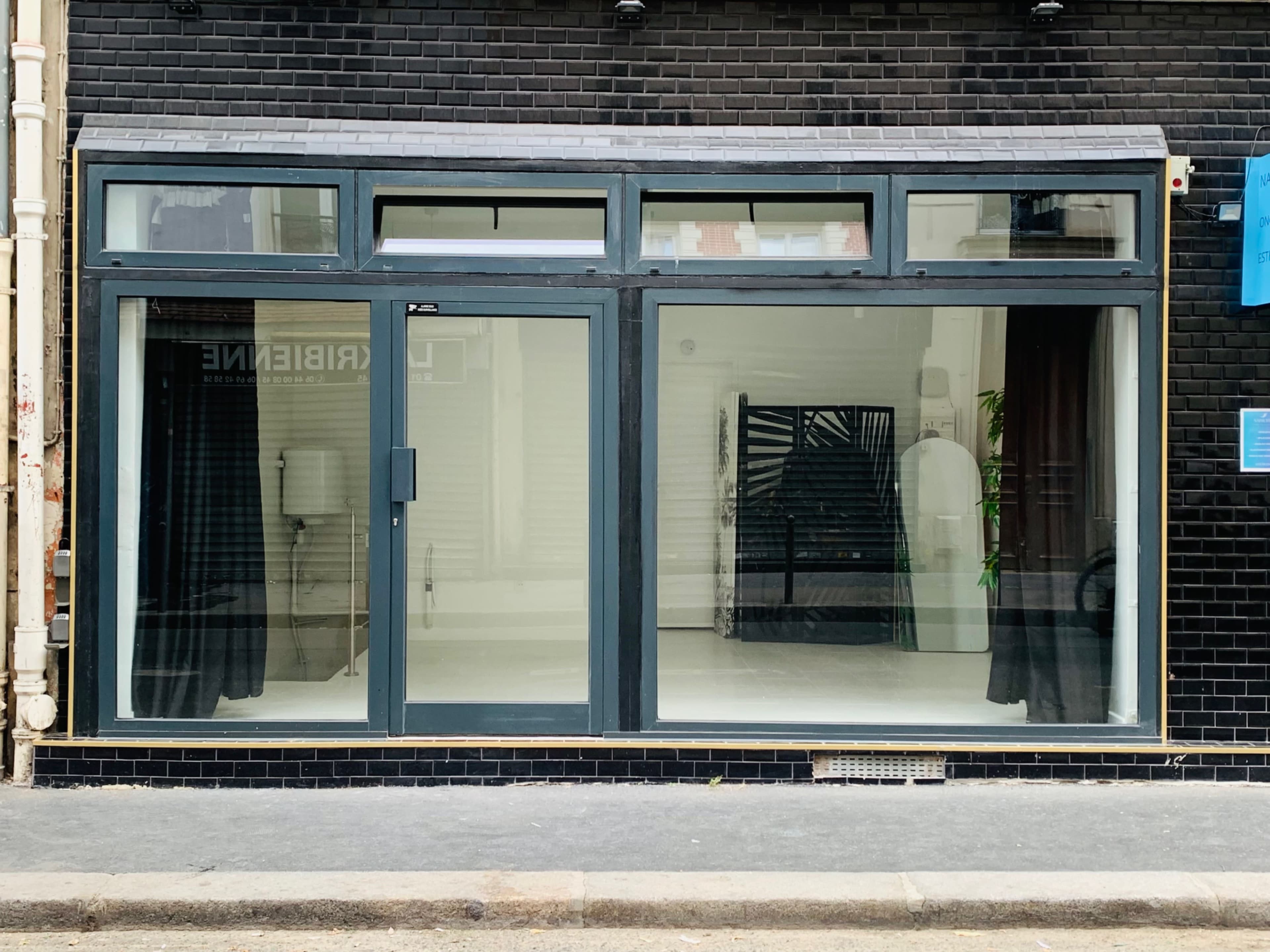 The image shows a storefront with large glass windows framed in dark blue, displaying an empty interior with a black partition and two curtains.