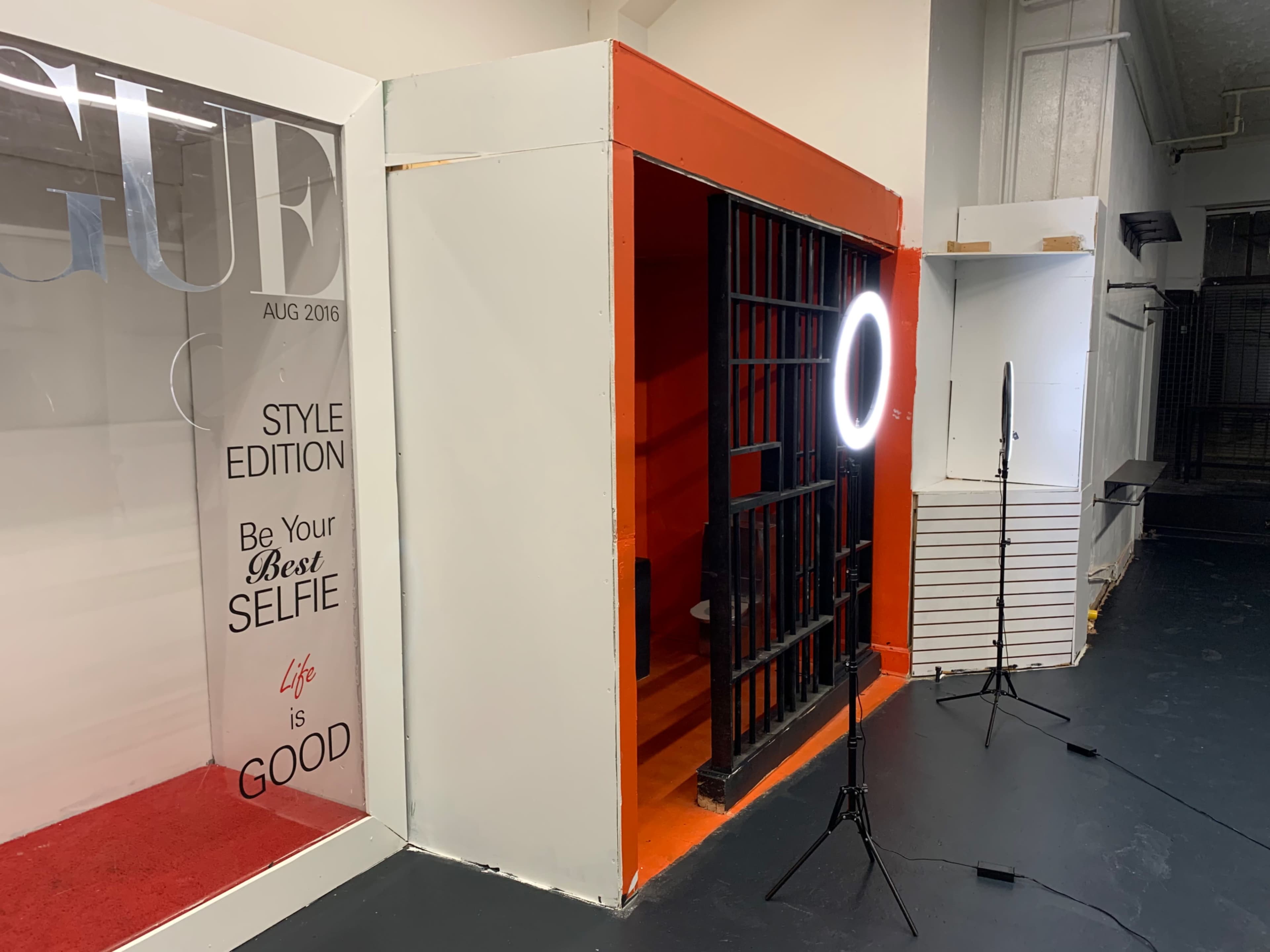 A stylized photo booth area with a vibrant orange backdrop, a ring light, and a magazine cover displayed nearby.
