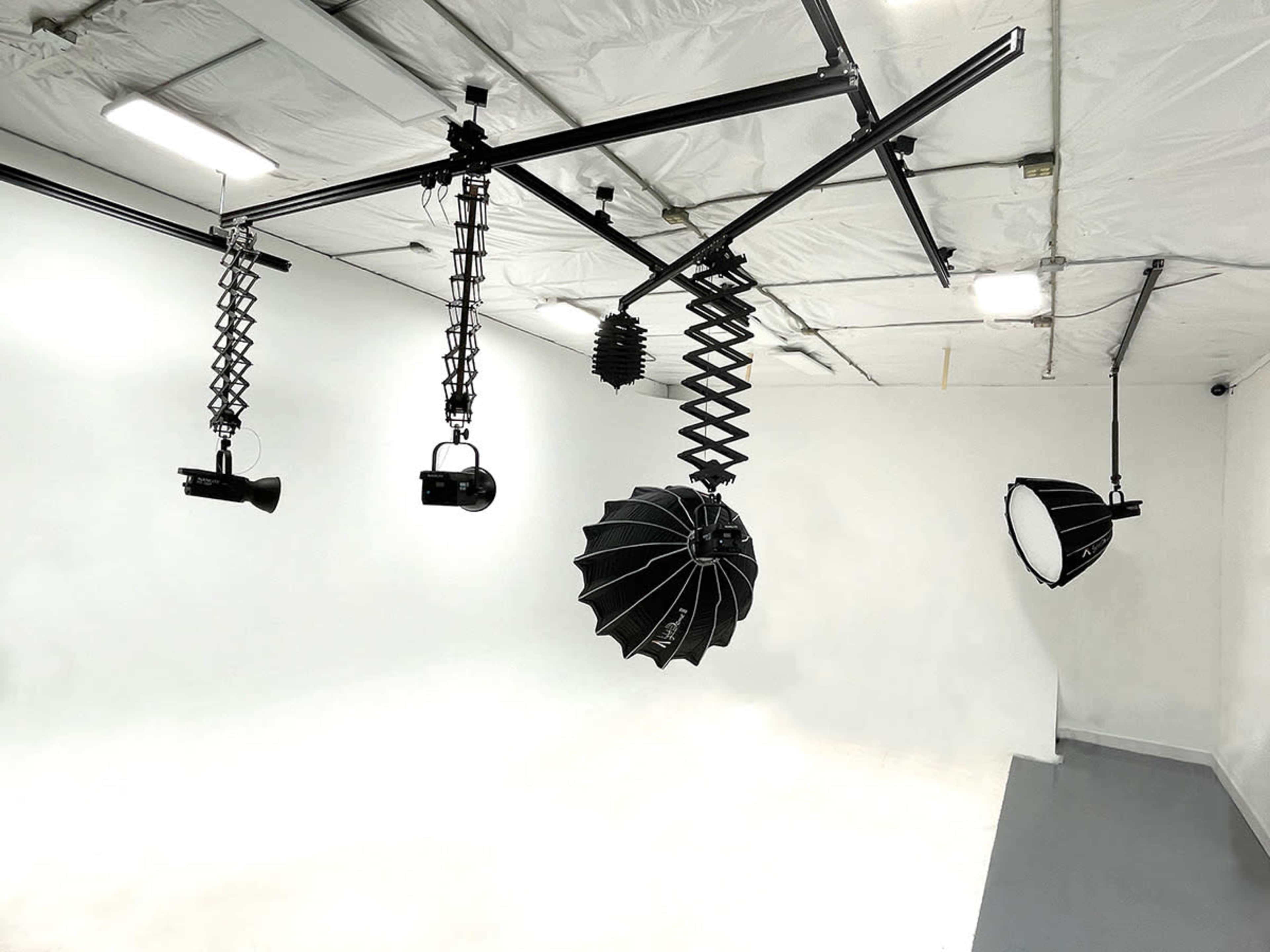 A photography studio with various lighting equipment suspended from a ceiling rig in front of a white backdrop.