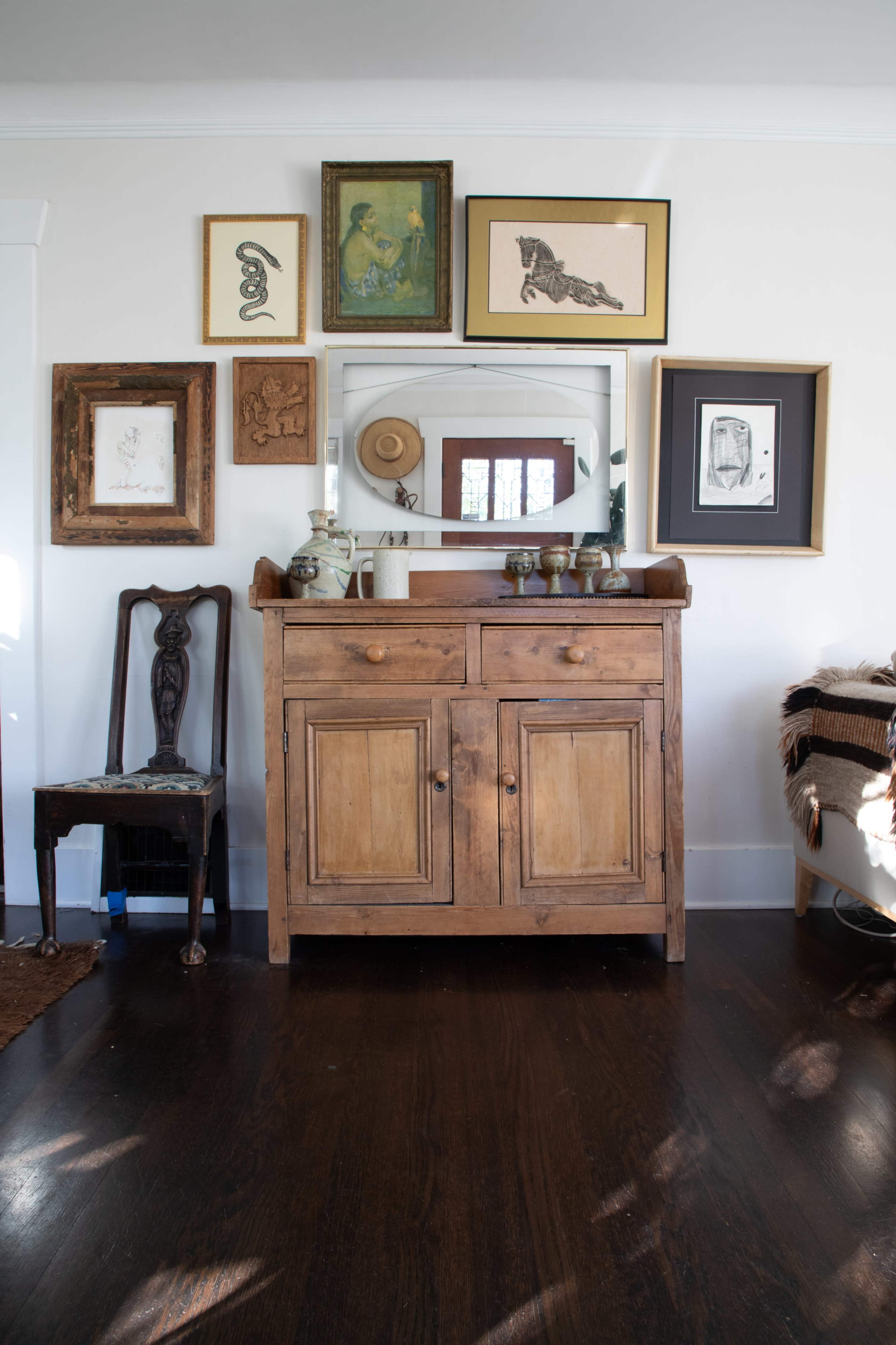 A wooden sideboard with two drawers and two doors is displayed against a wall adorned with various framed artworks and a mirror.