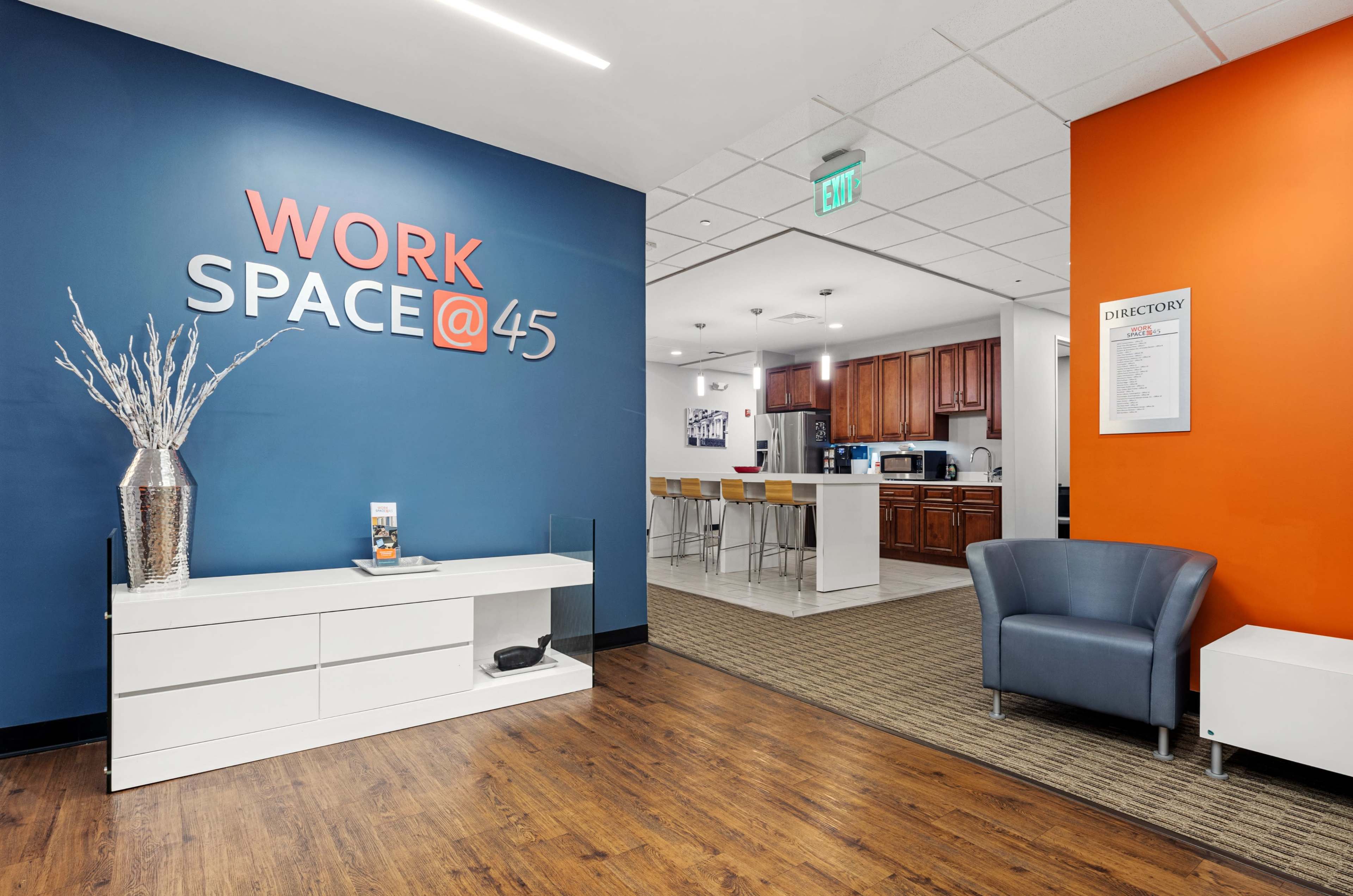 A modern office space with a blue and orange accent wall, a reception area with a sleek console table, and a kitchen area in the background.