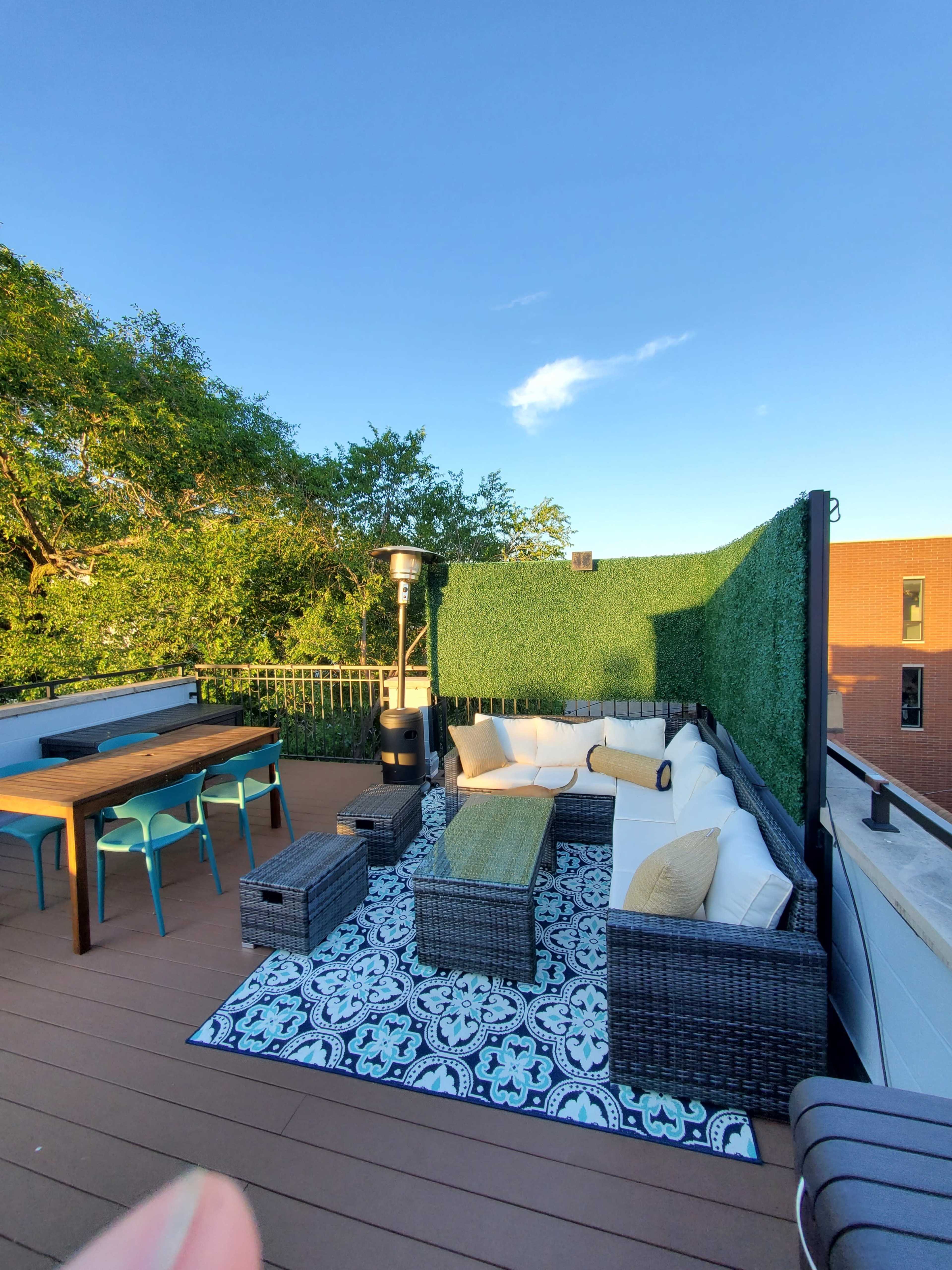 A rooftop terrace with a seating area, a dining table, and greenery along the perimeter.