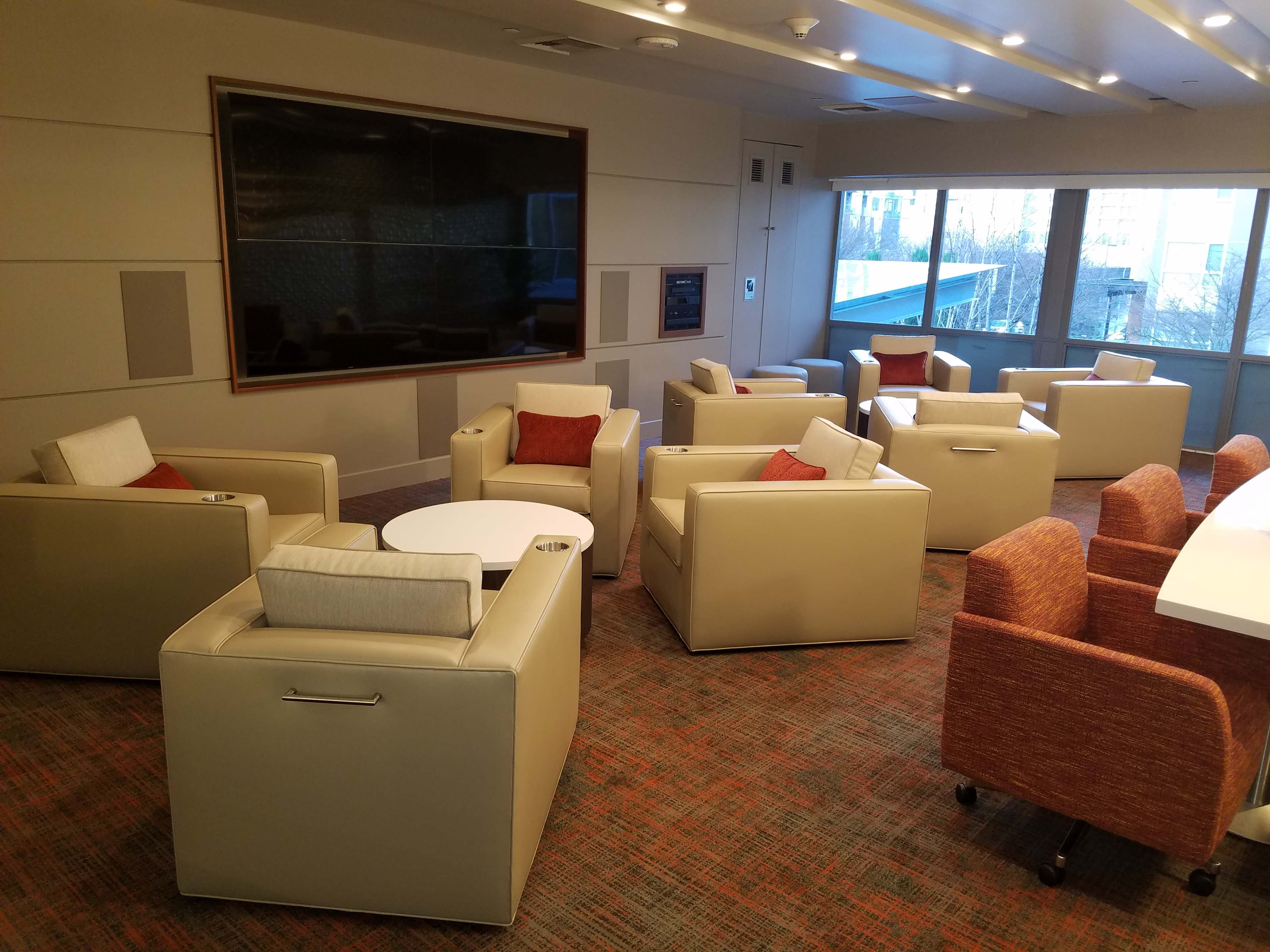 A modern lounge area with beige armchairs and a round coffee table arranged around a large window.