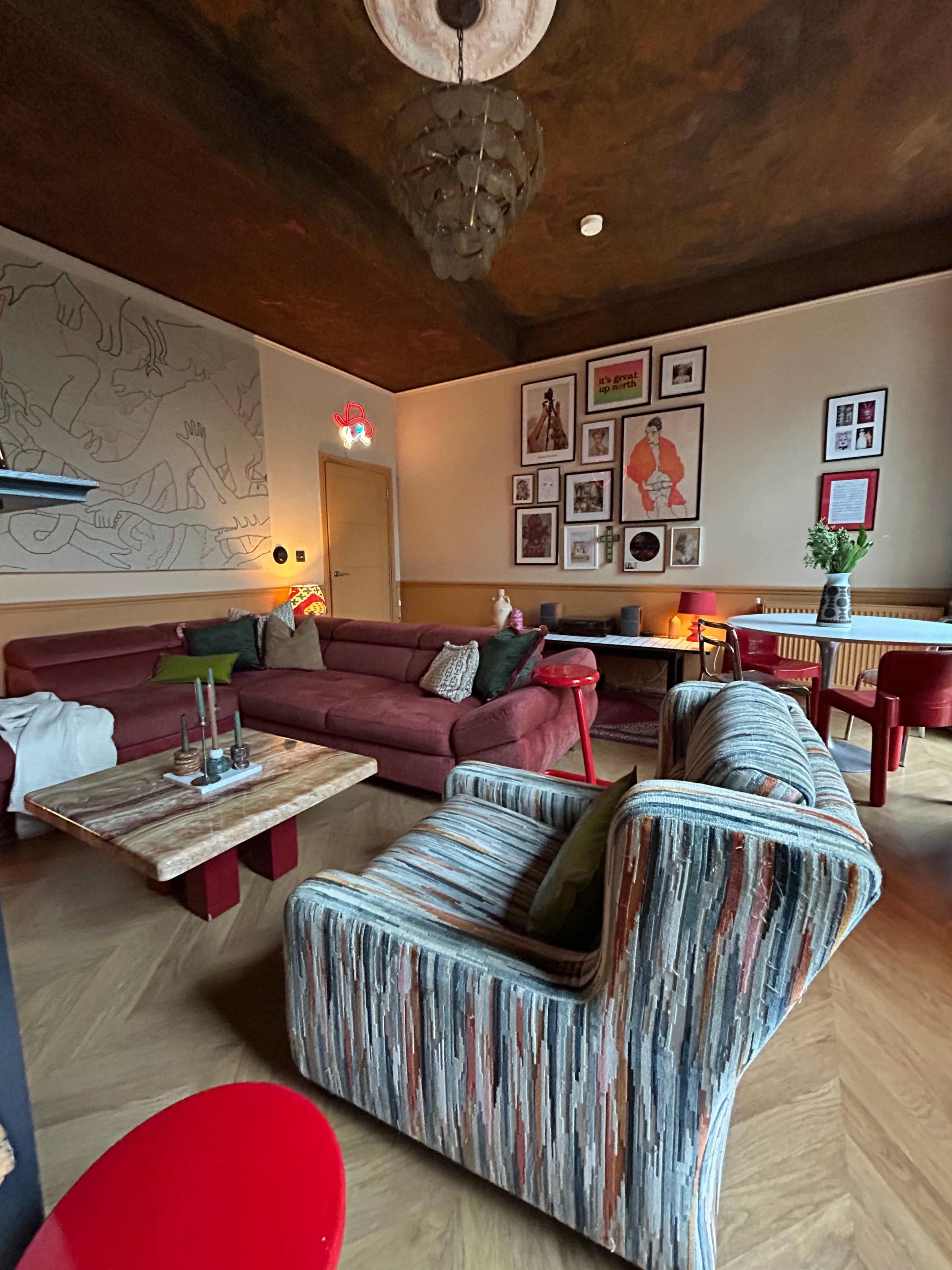 A cozy lounge area features a mix of colorful seating, a wooden coffee table, and eclectic wall art.