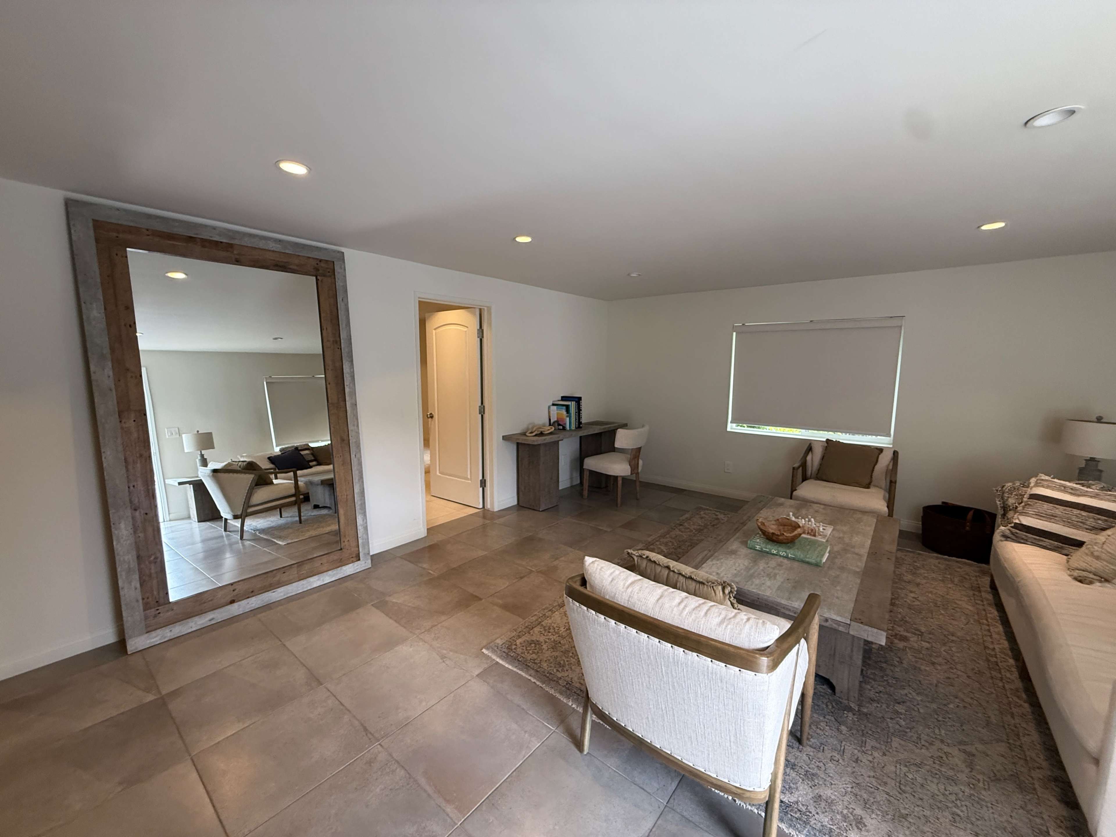 The image shows a modern living space with a large mirror, a sofa, a coffee table, and a desk against a light-colored wall.