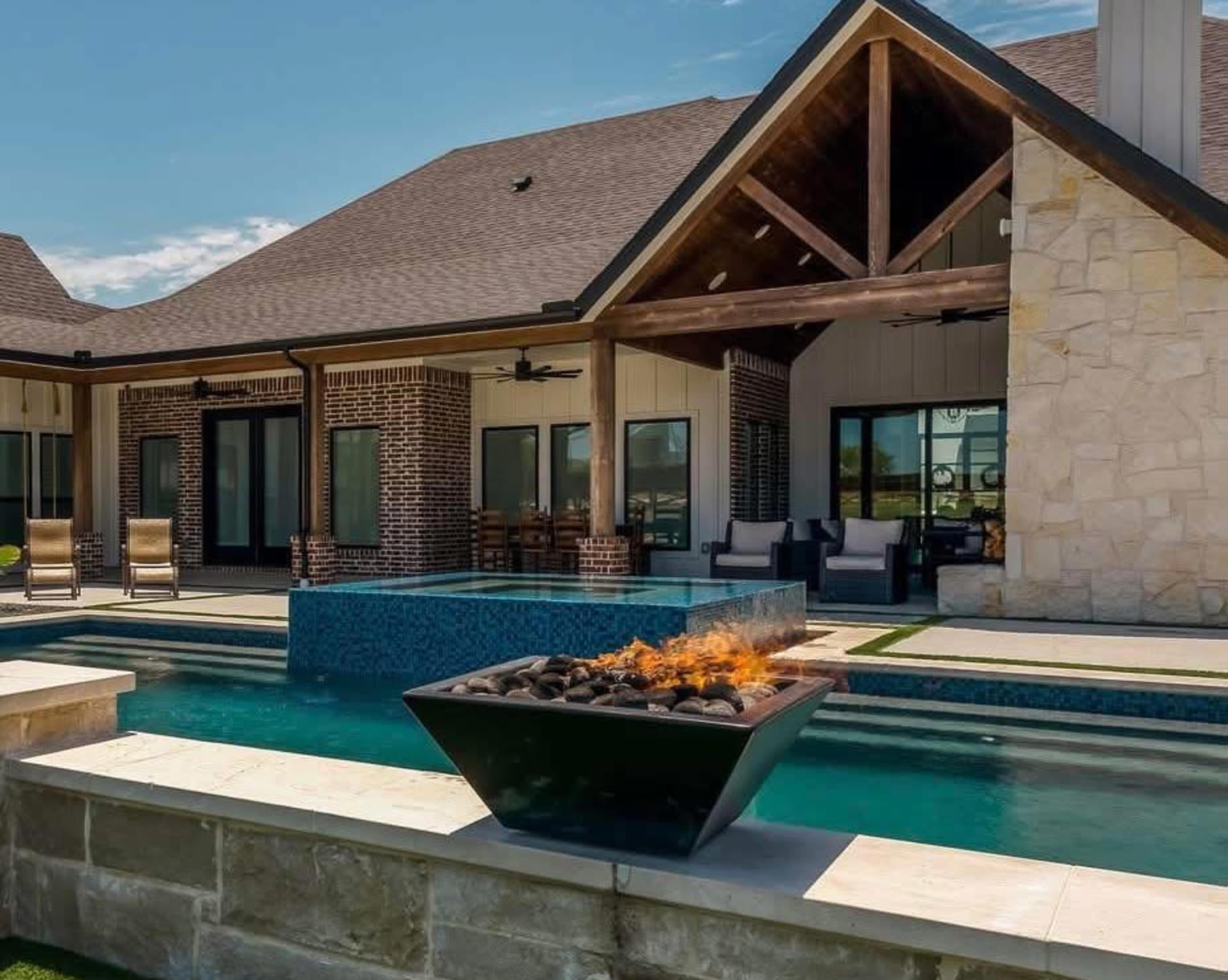 The image shows a modern backyard with a swimming pool, a stone fire pit, and a stylish house featuring a gabled roof.