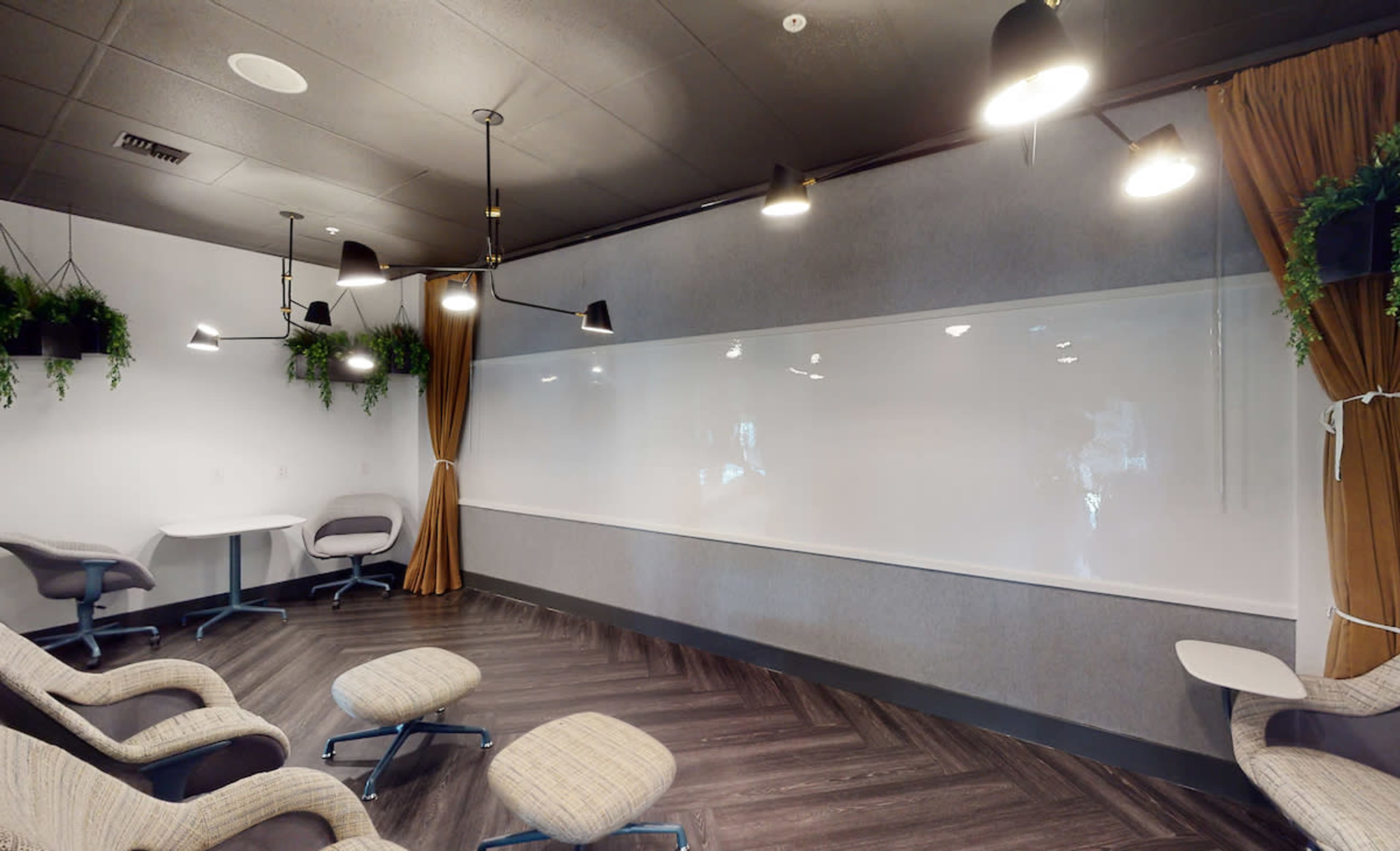 A modern meeting room featuring a large whiteboard, comfortable seating, and pendant lights.