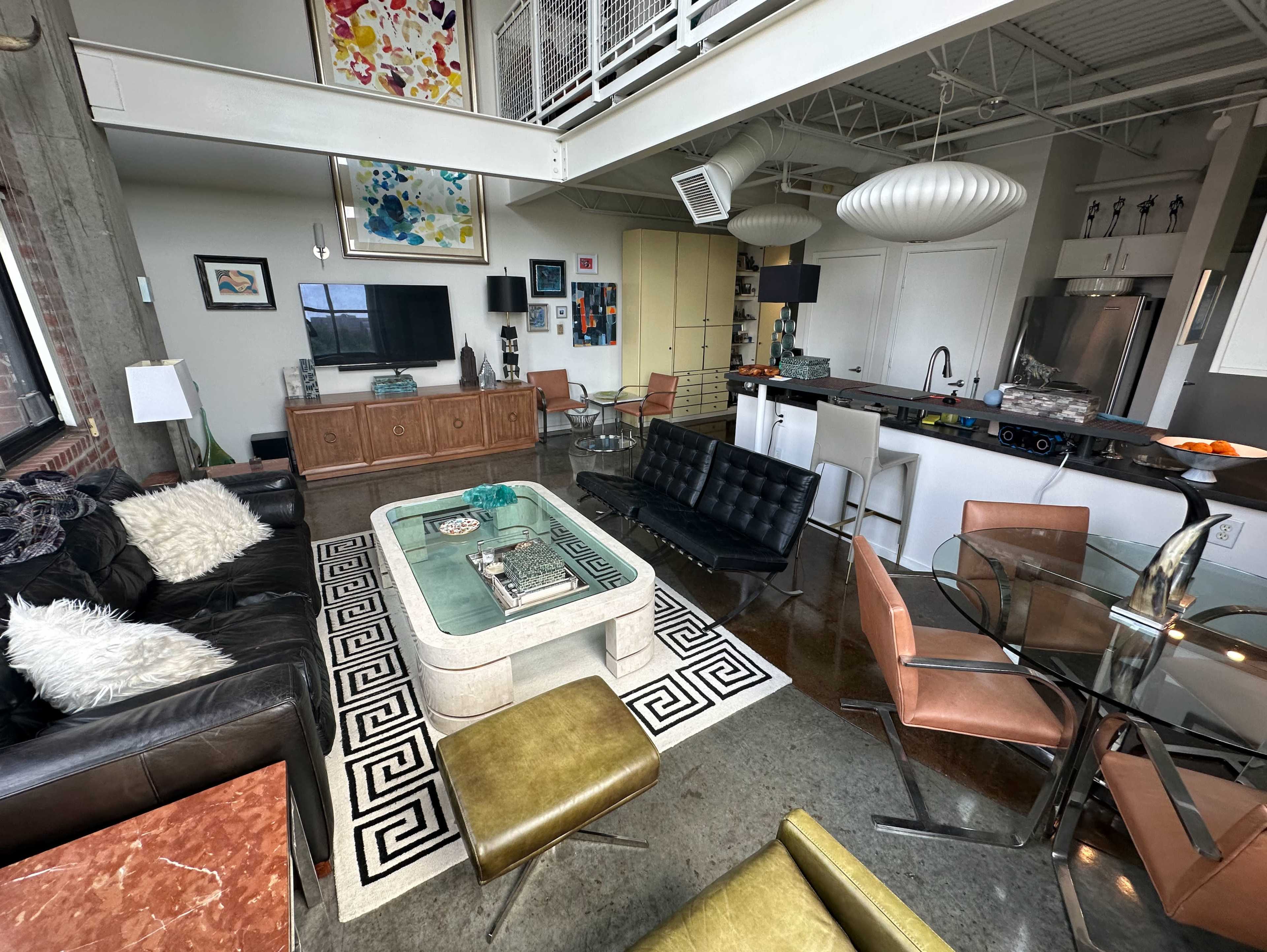 The image shows a modern, open-concept living space with a mix of furniture, including a black sectional sofa, glass dining table, and a neutral-colored rug.