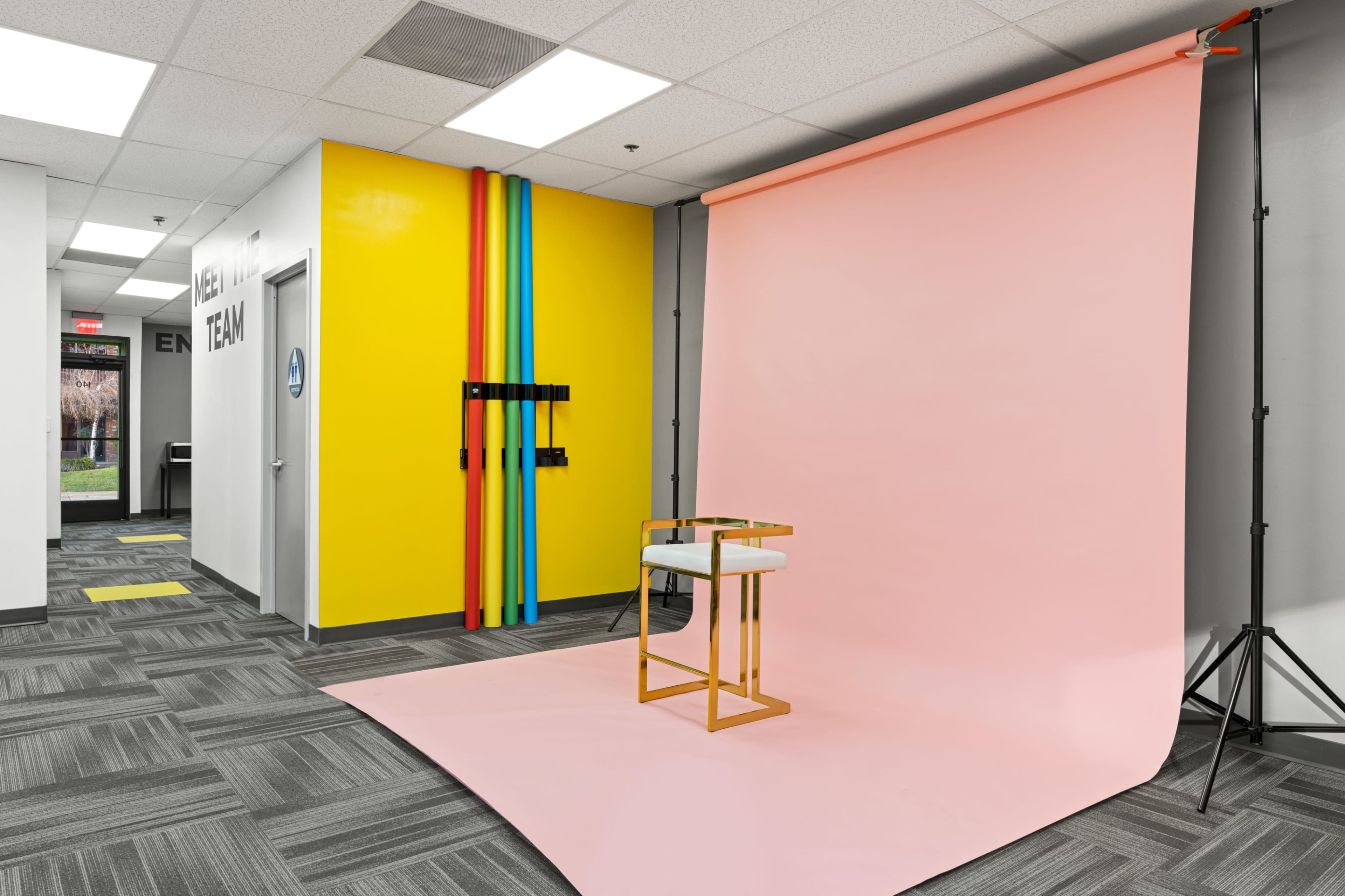 A pink background is set up in a brightly colored room with a chair placed in front of it, near a door labeled "TEAM."