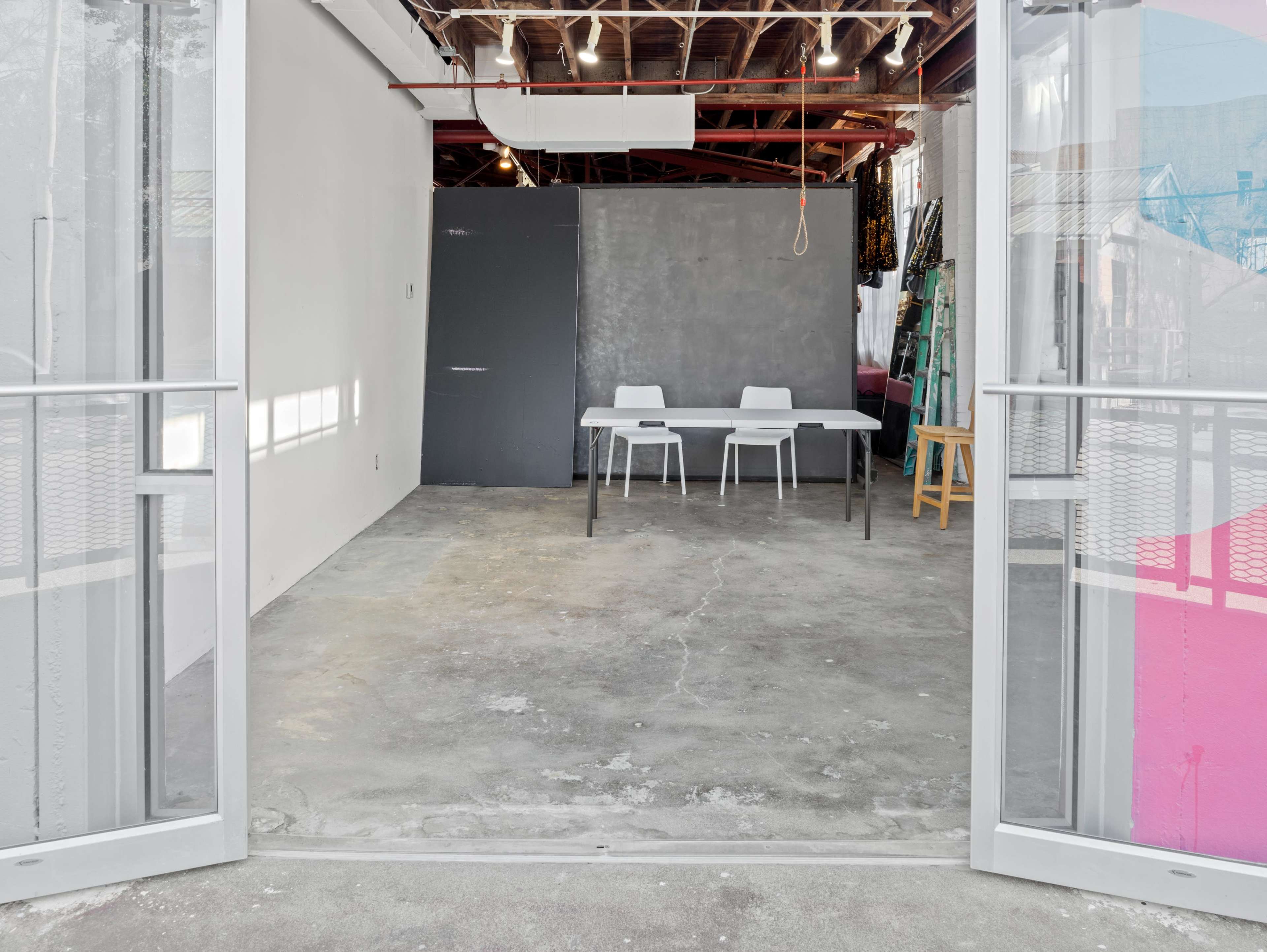 A spacious, empty room with a concrete floor, featuring a table and two chairs, viewed from an open doorway.