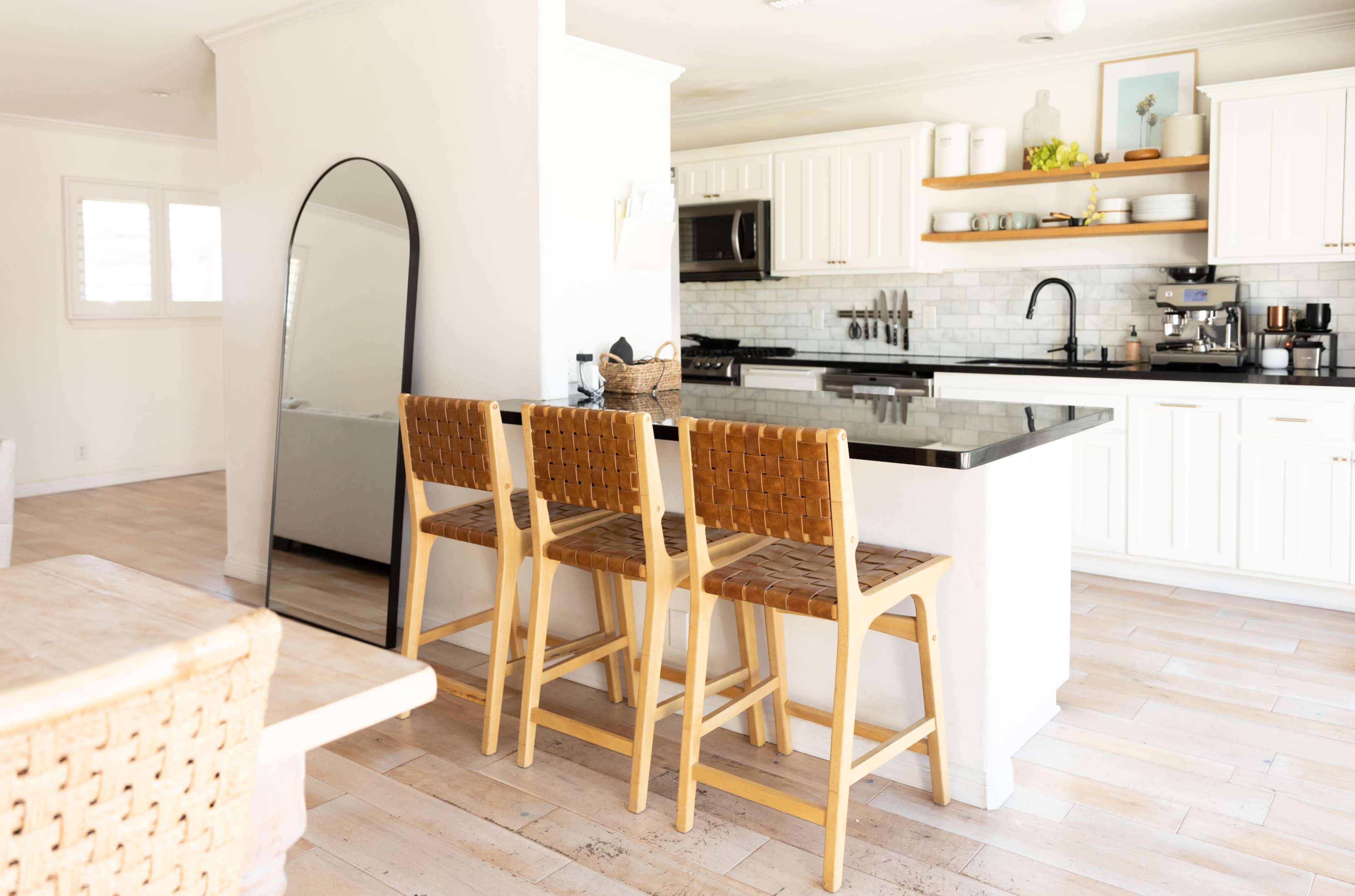 A modern kitchen features a black countertop with wooden bar stools, white cabinetry, and stainless steel appliances.