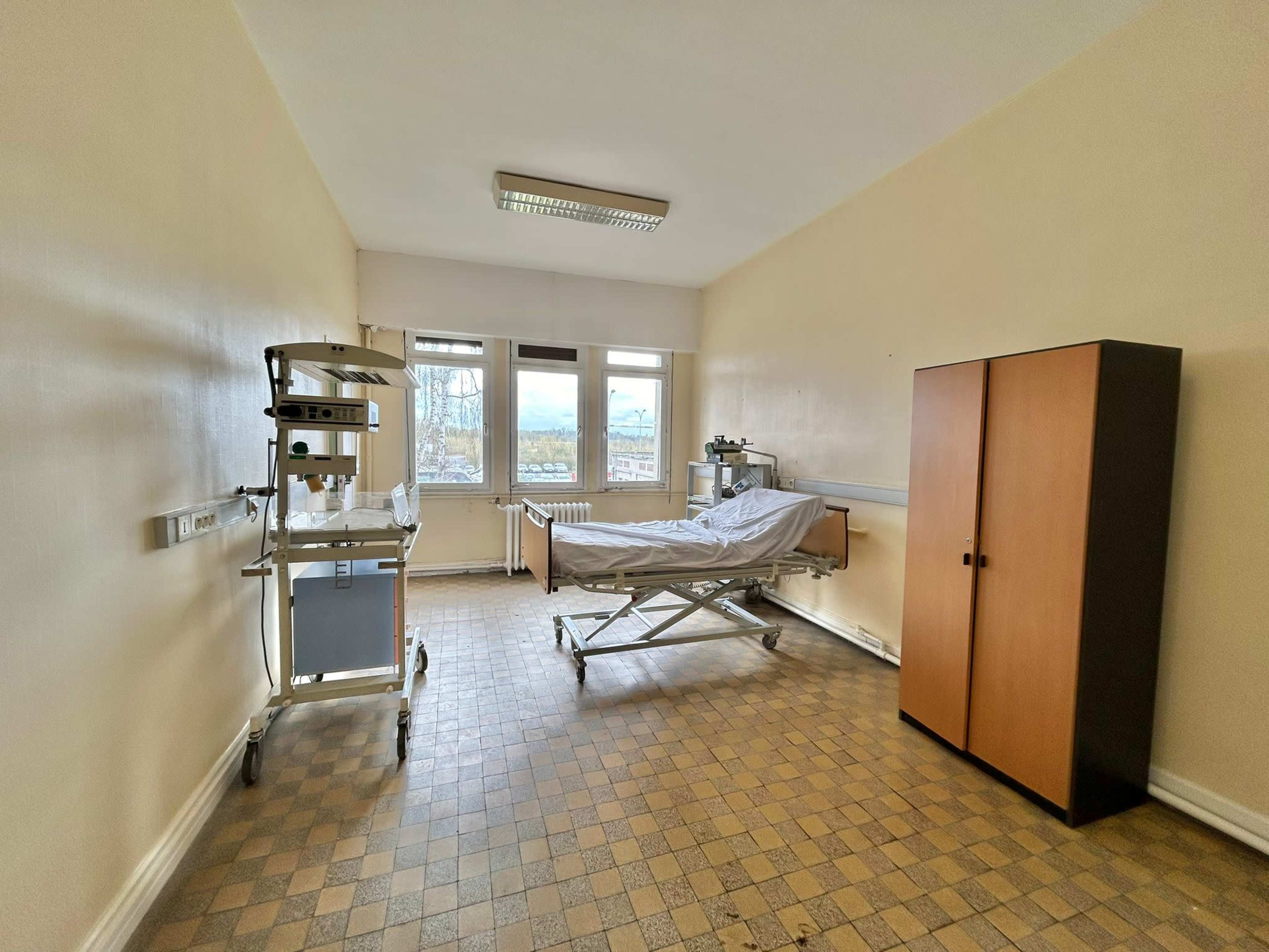 A hospital room with a bed, medical equipment on a stand, and a cabinet.