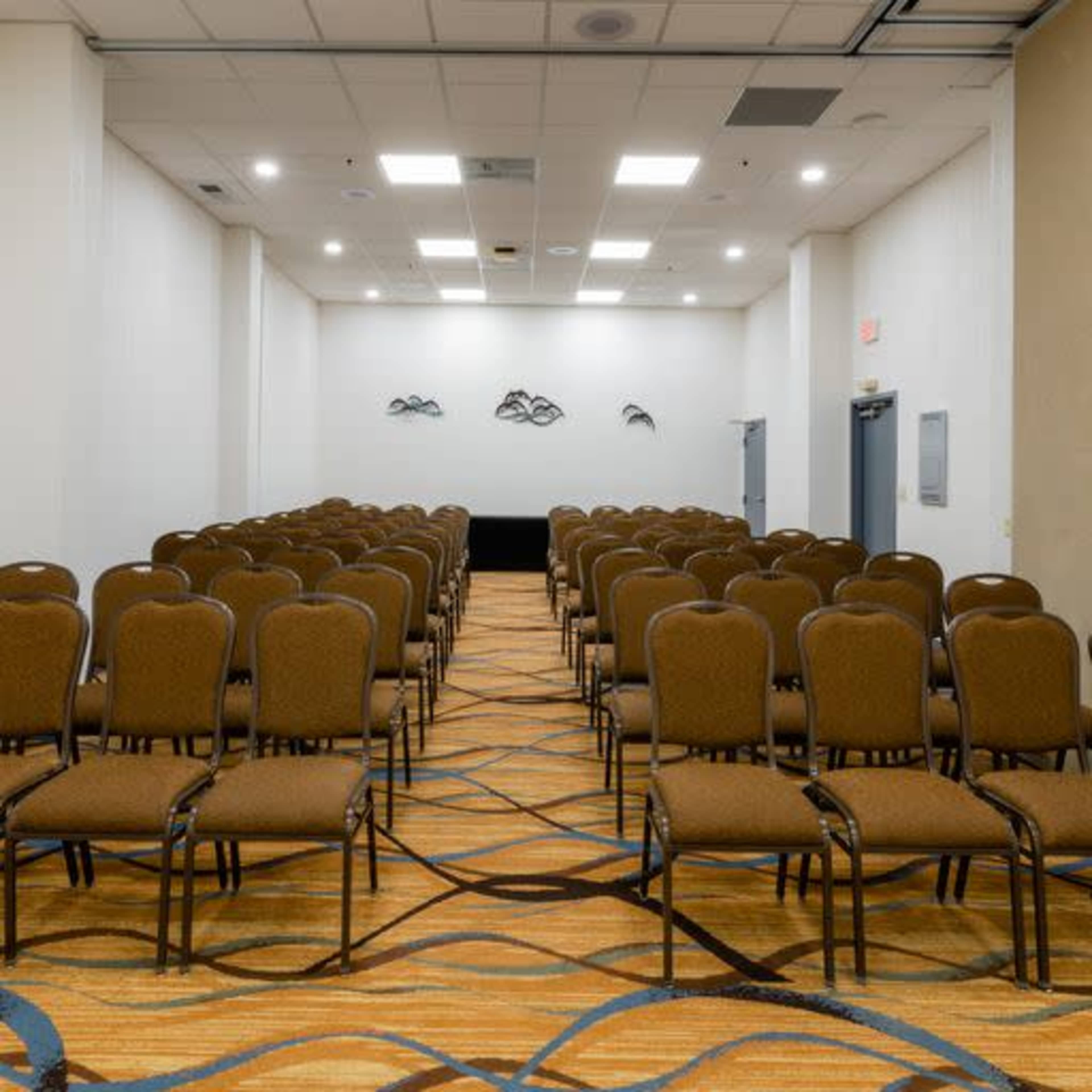 A seminar room with rows of empty brown chairs arranged in a grid pattern on a carpeted floor.