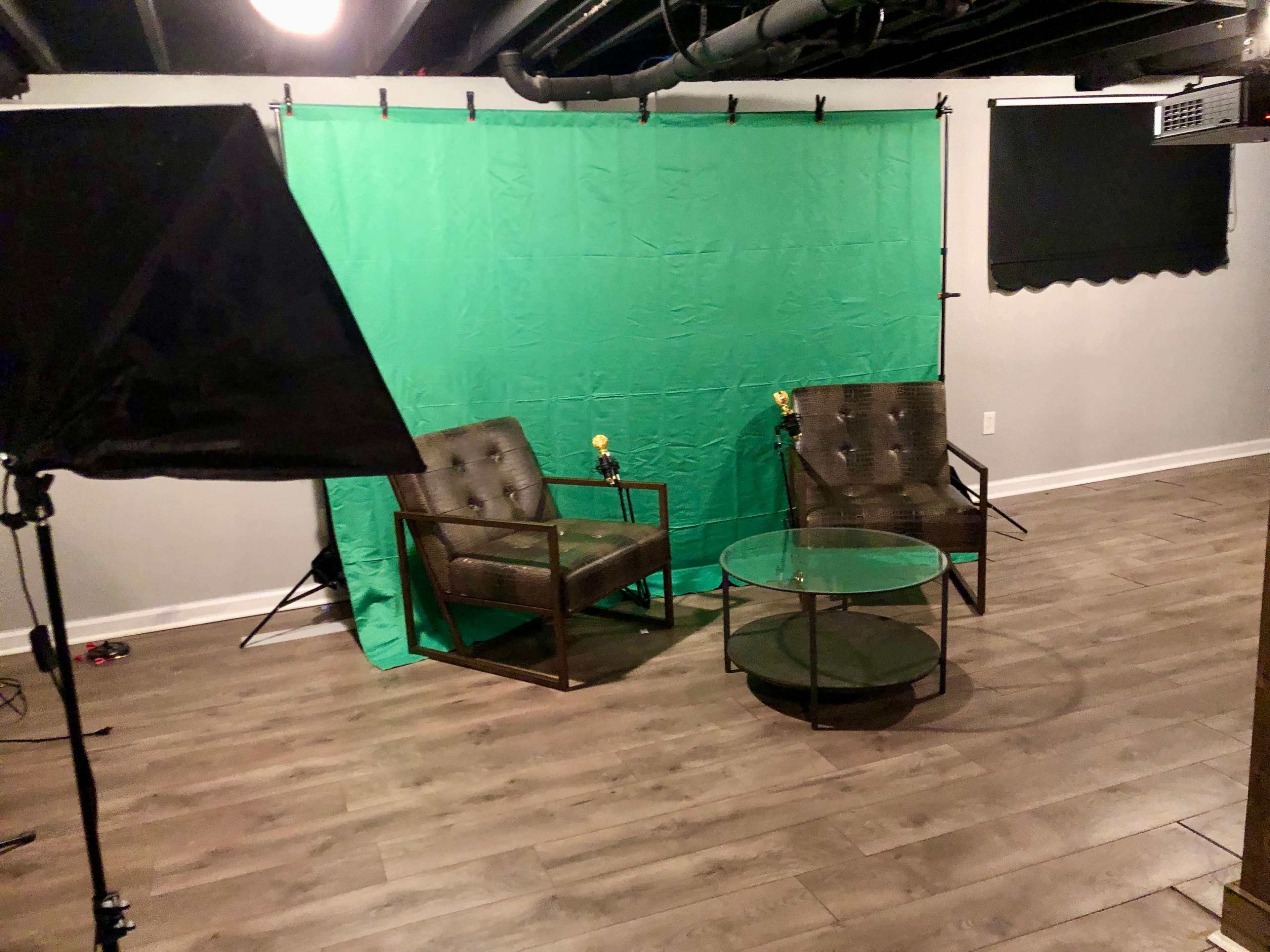 A studio setup with two chairs, a glass table, and a green backdrop, illuminated by softbox lighting.