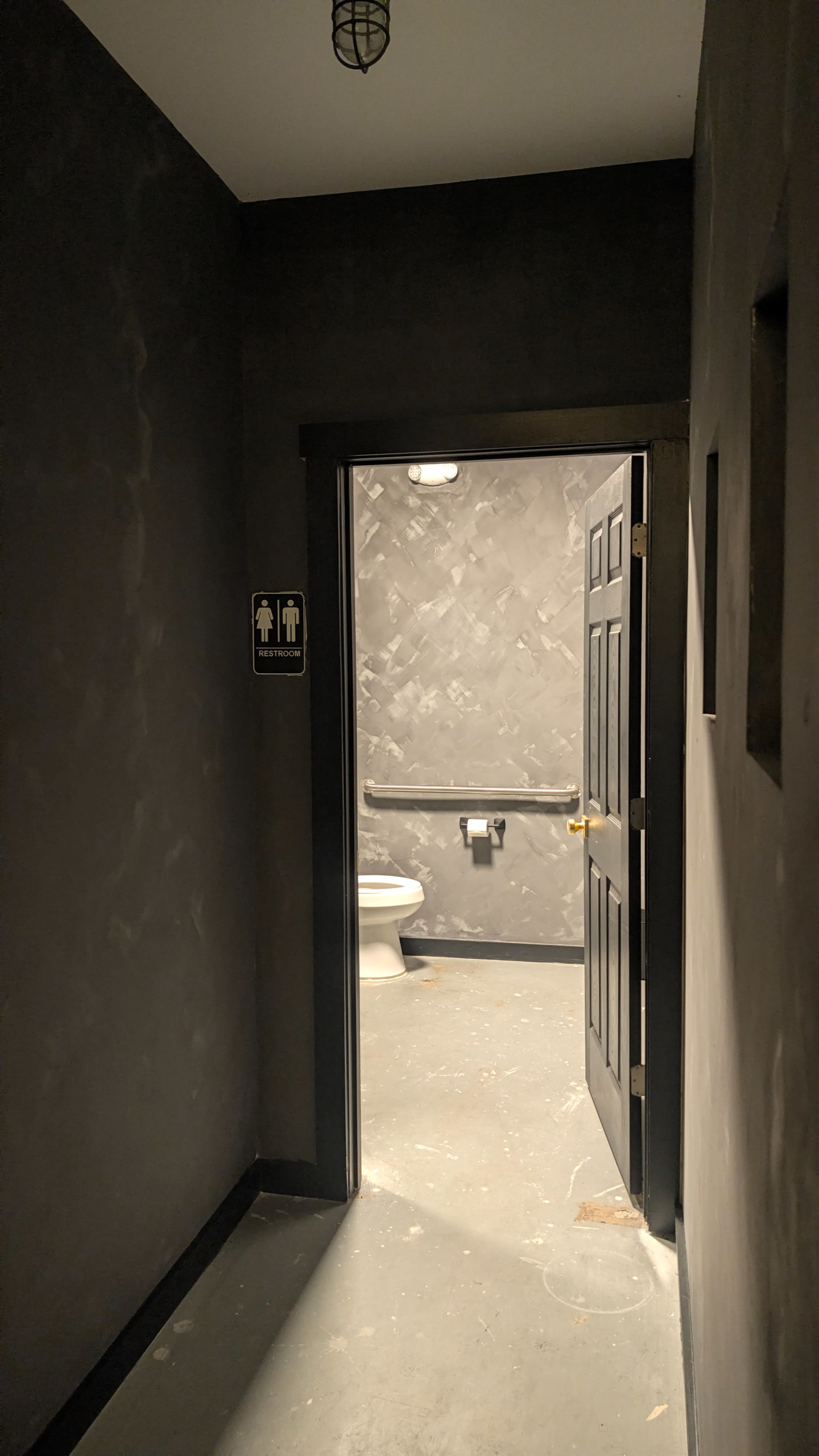 A dimly lit hallway leads to a restroom with a visible toilet in the background.