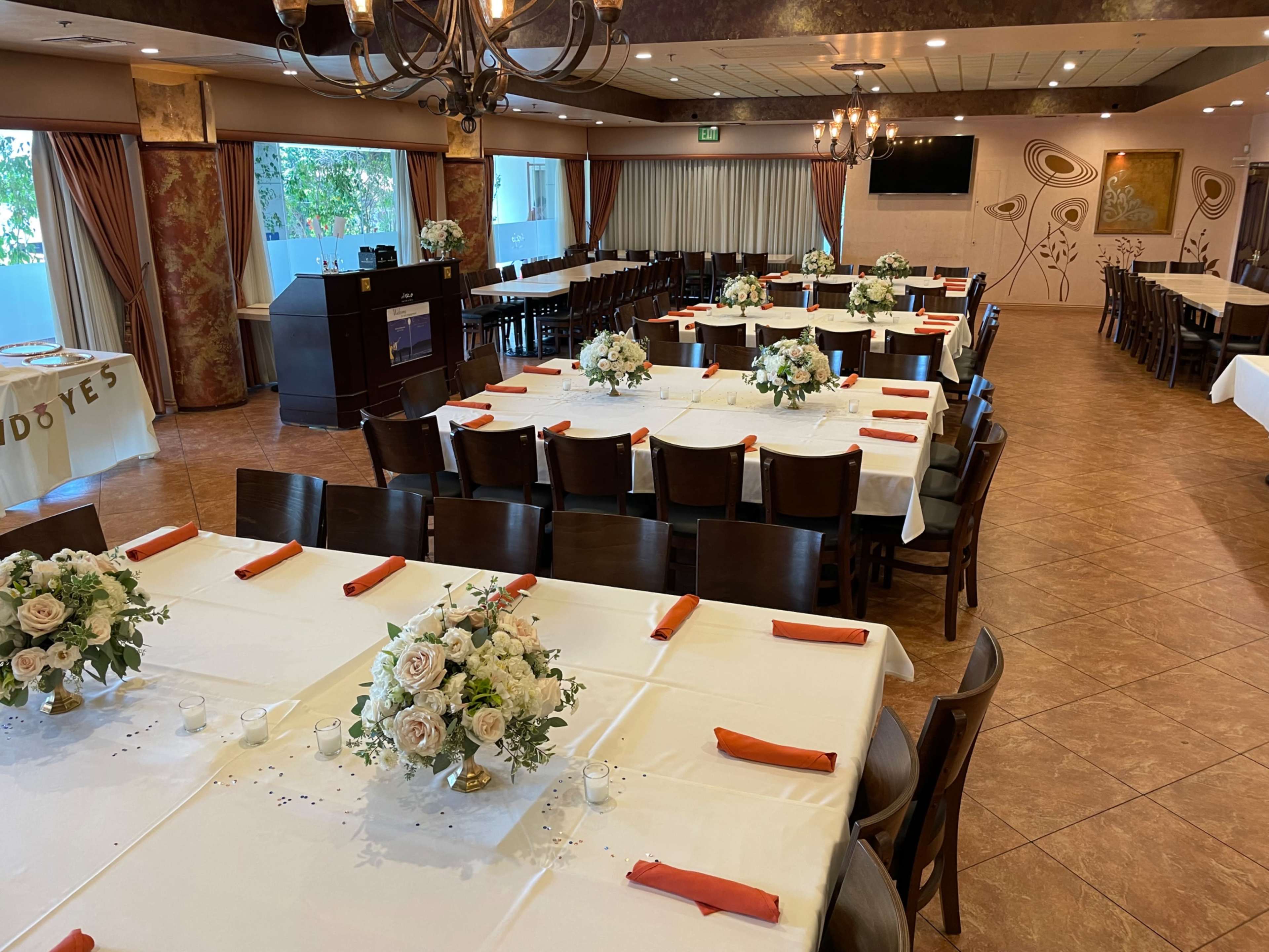 A dining hall with several long tables set with white tablecloths and floral centerpieces, arranged for an event.