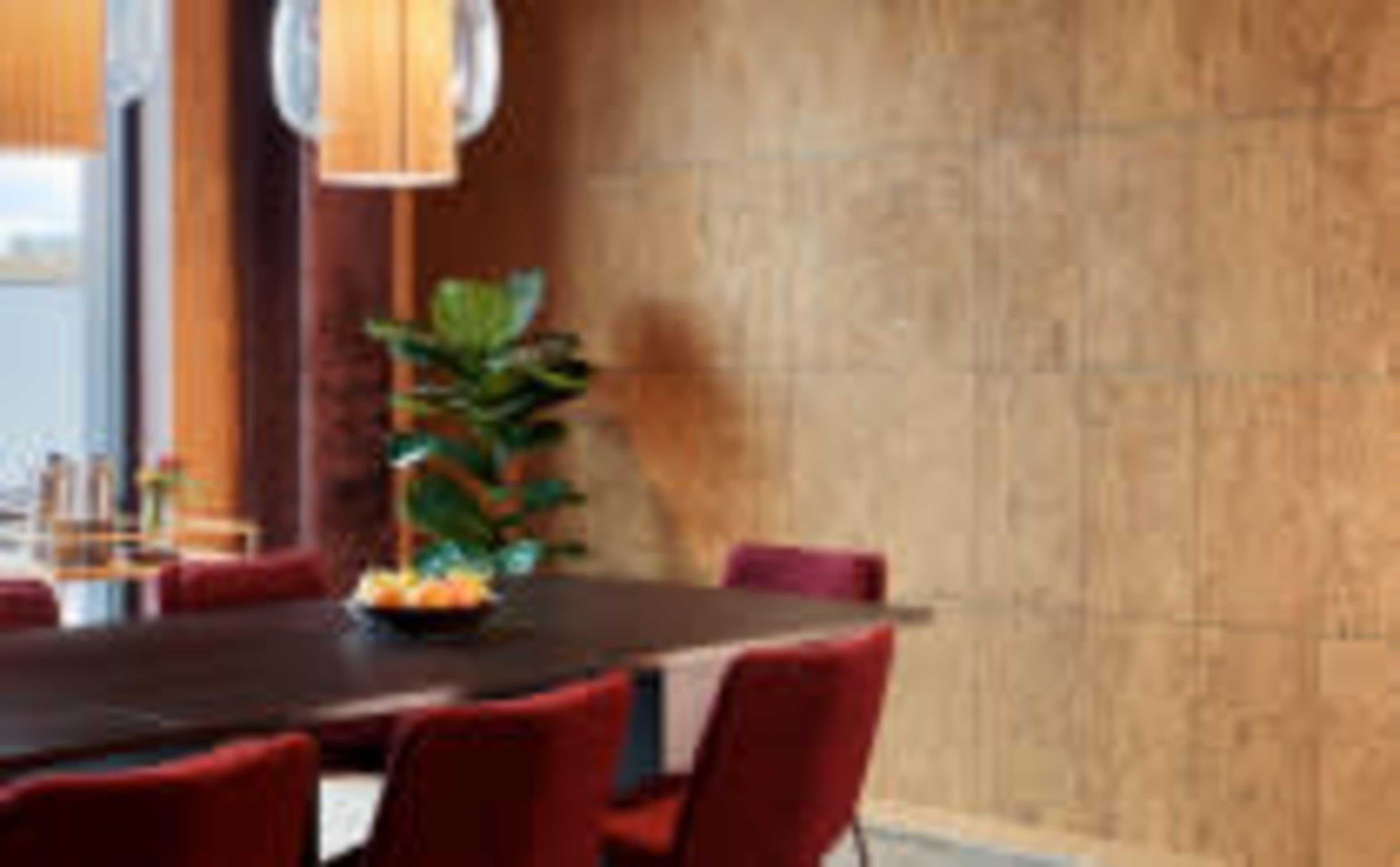 A dining area features a dark table surrounded by red chairs, with a plant and a pendant light illuminating the space.