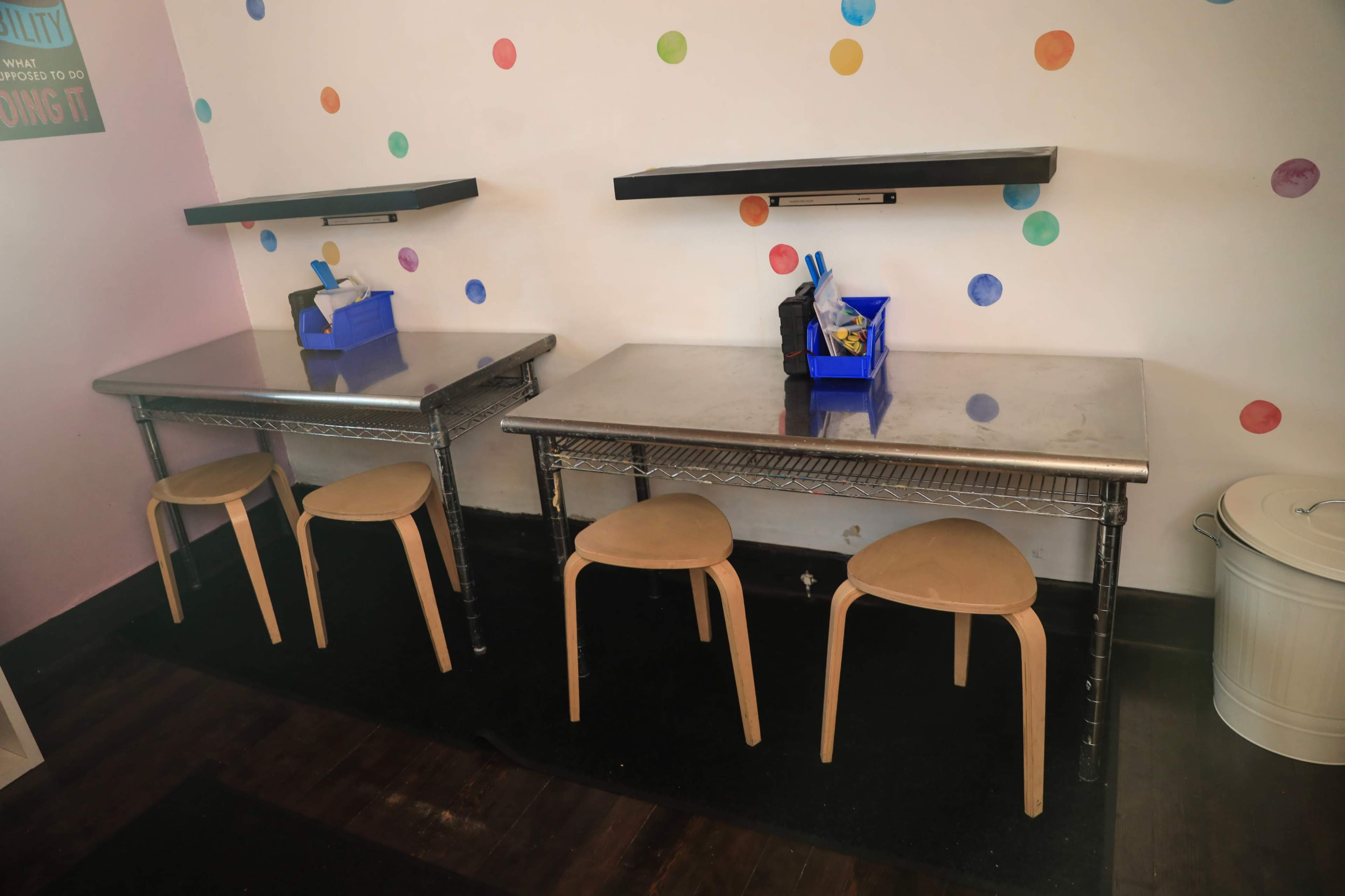 Two metal tables with chairs sit on a dark floor against a wall decorated with colorful dots.