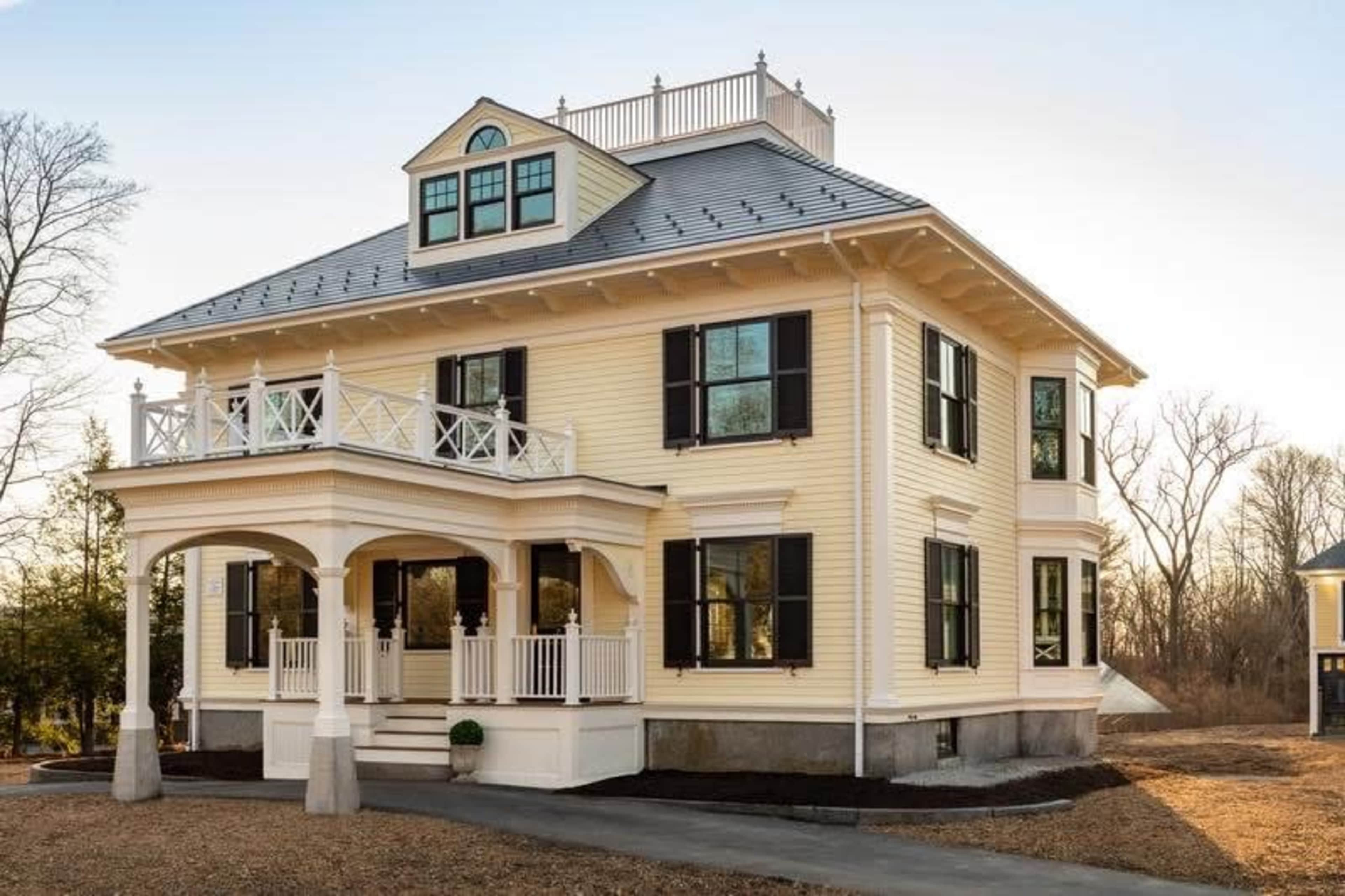 The image shows a large, two-story yellow house with a front porch, multiple windows, and a rooftop deck.