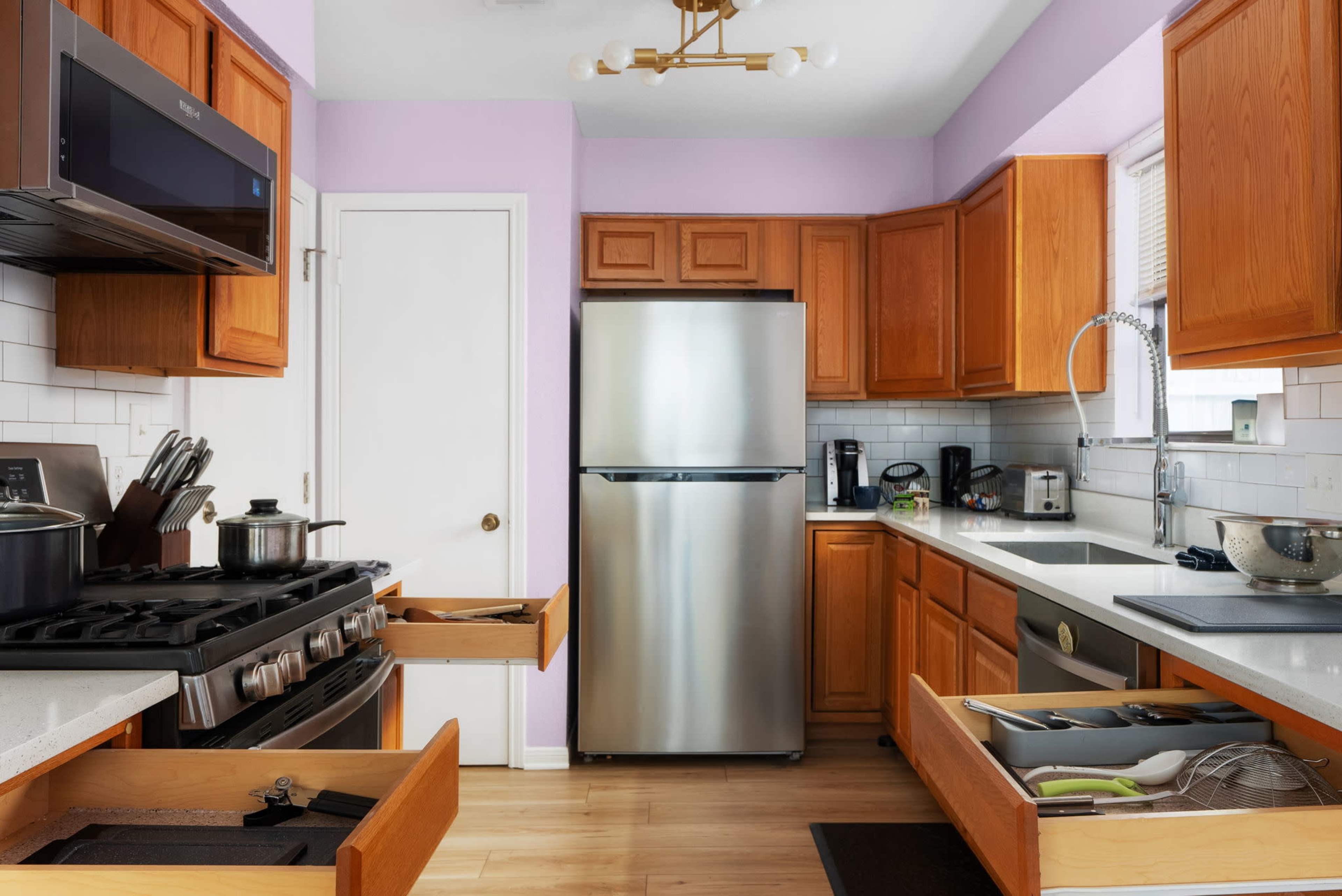 A modern kitchen features wooden cabinetry, stainless steel appliances, and an open layout with countertops and drawers partially pulled out.