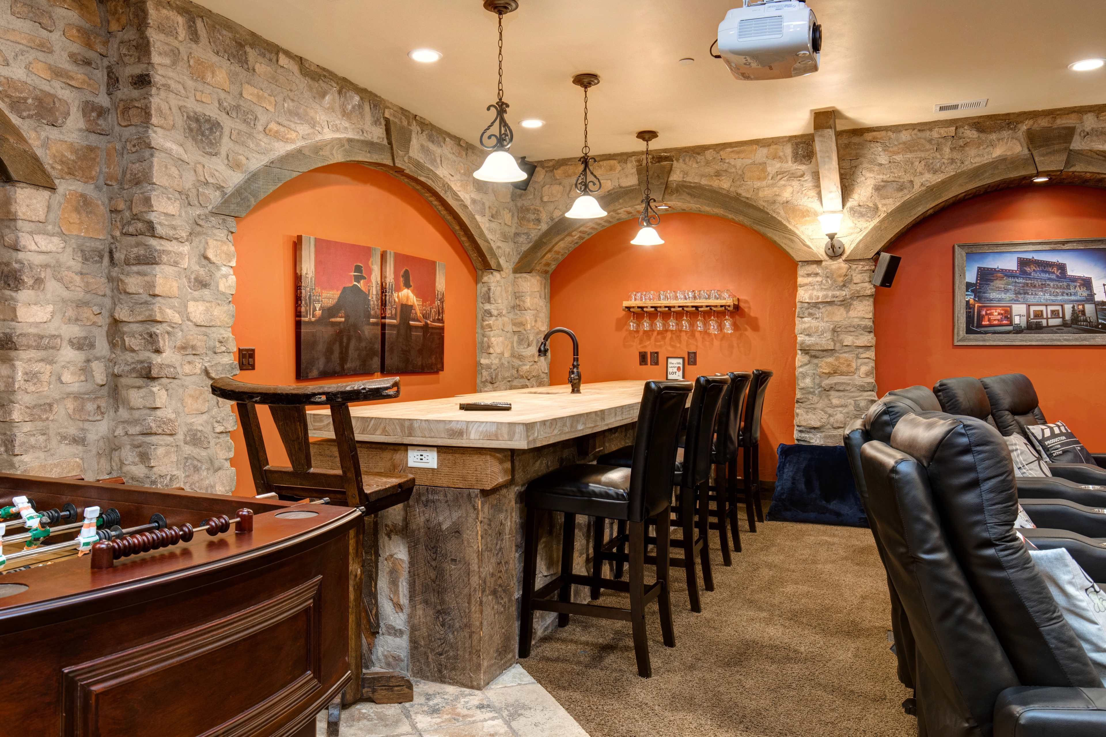 A home entertainment room with a stone wall, a bar area with high stools, and a seating arrangement featuring black reclining chairs.