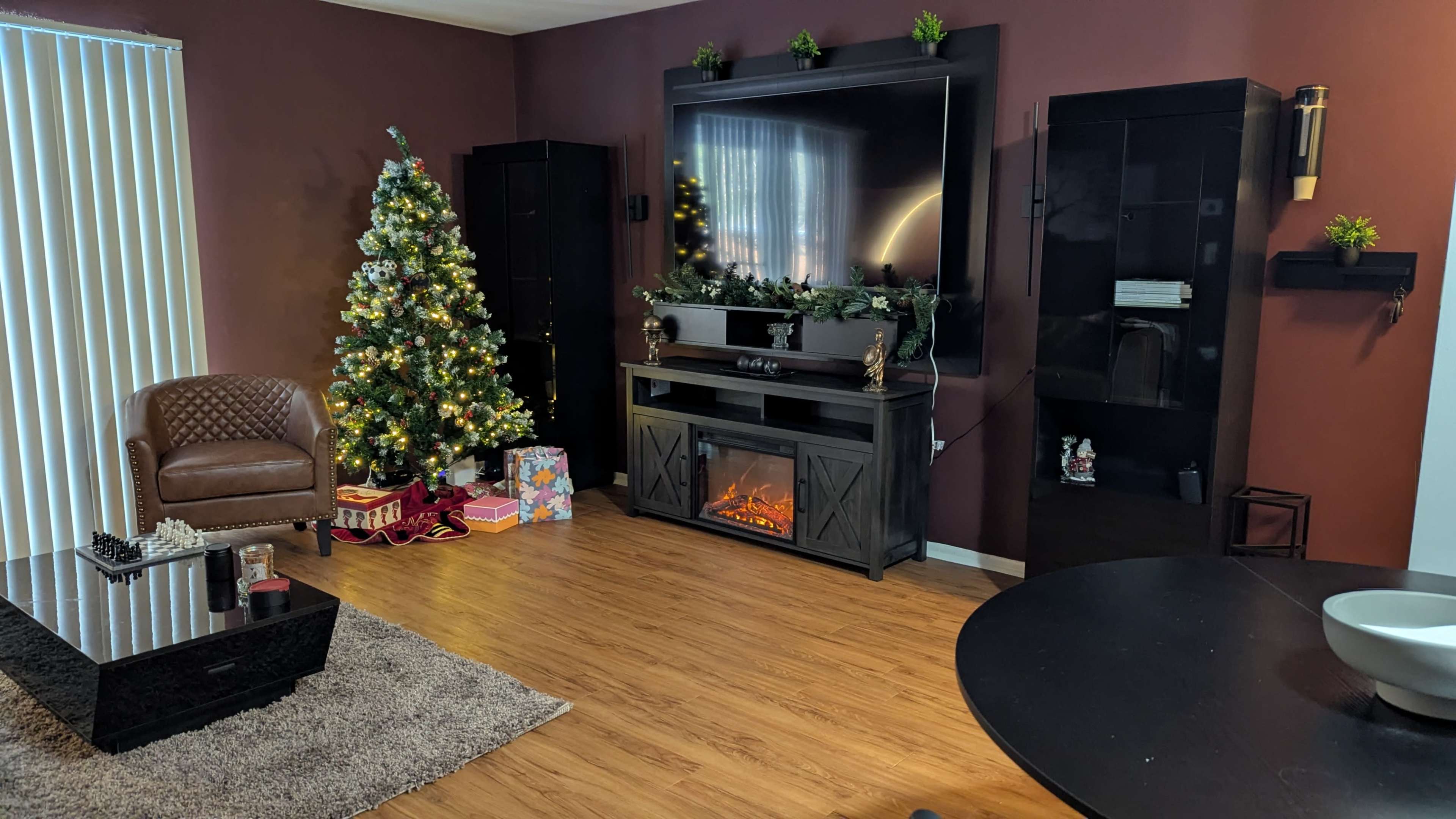 The living room features a Christmas tree beside a modern entertainment center with a faux fireplace and a dark wood dining table.