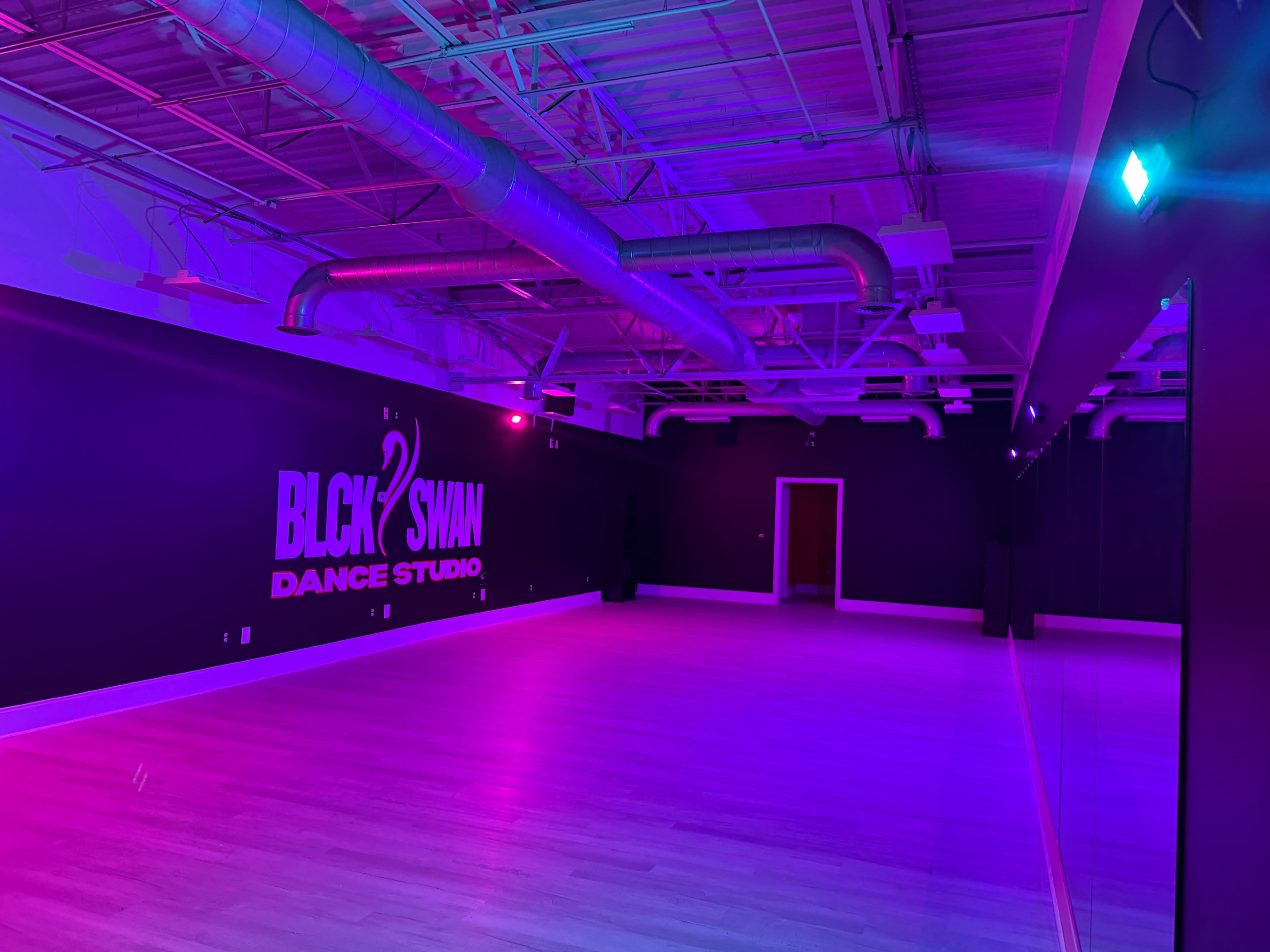 The image shows the interior of a dance studio with purple and blue lighting, featuring a mirrored wall and the name "BLCK SWAN DANCE STUDIO" displayed on the wall.