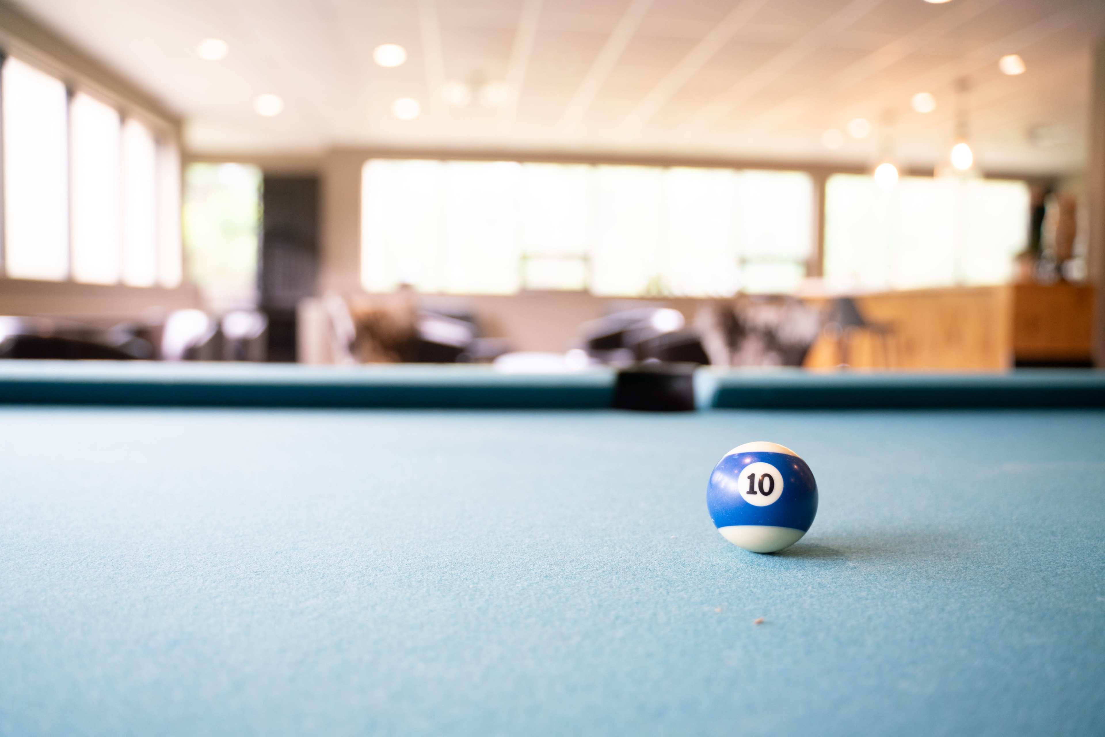 A blue and white billiard ball with the number 10 rests on a green felt pool table in a brightly lit room.