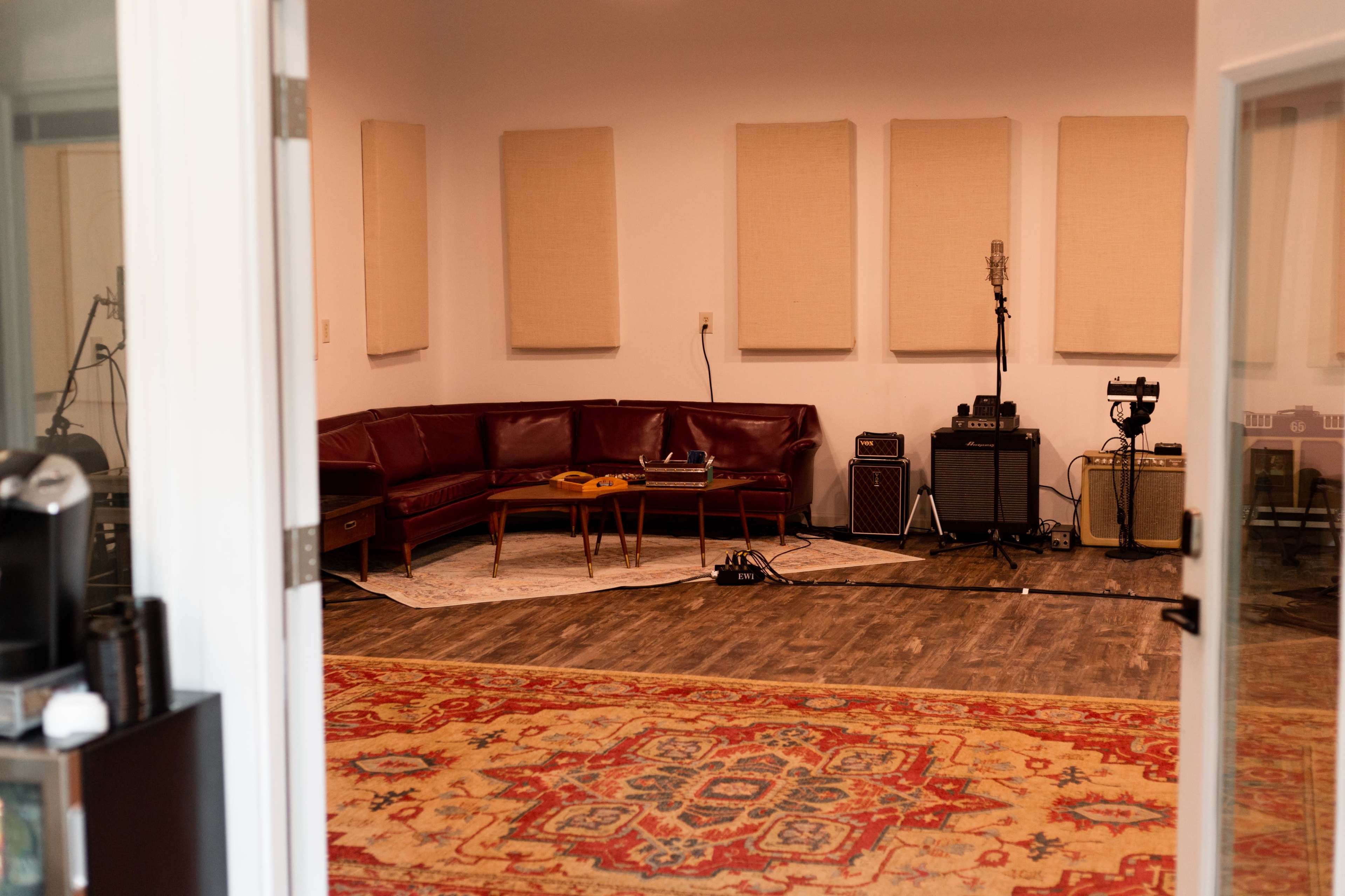 A music recording studio with a red leather couch, microphones, amplifiers, and soundproofing panels on the walls.